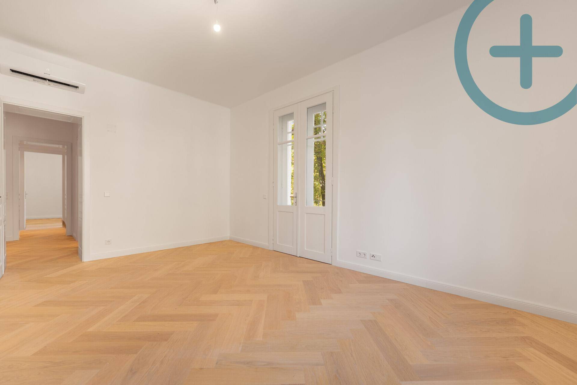 Helles Schlafzimmer mit Fischgrätparkett und Zugang zu einem französischen Balkon.