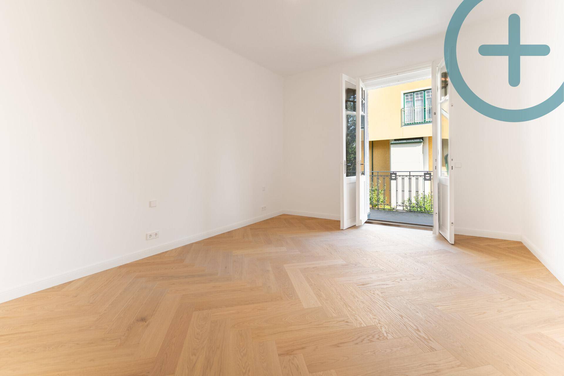 Heller Raum mit Fischgrätparkett und Zugang zu einem kleinen Balkon.