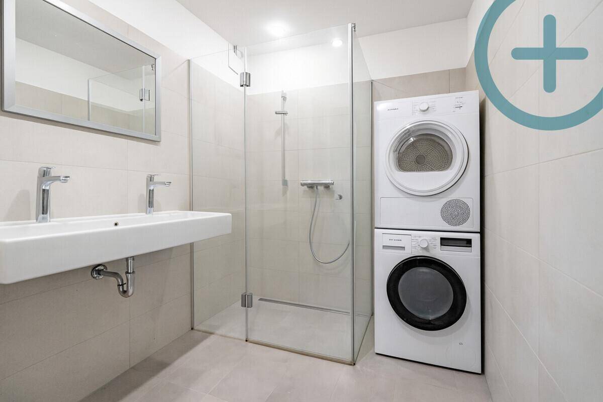 Modernes Badezimmer mit ebenerdiger Dusche, Doppelwaschbecken und Waschmaschine.