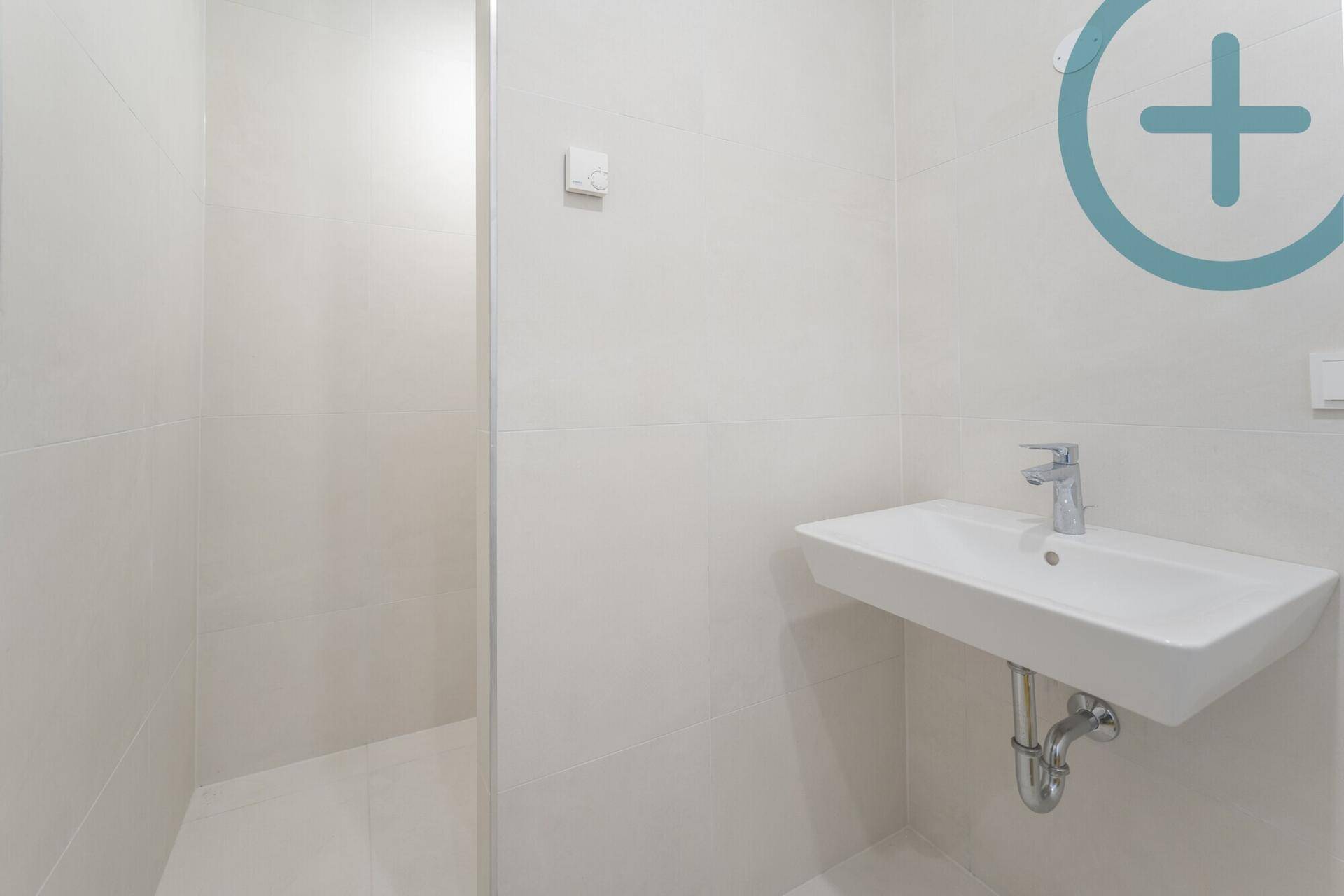 Modernes Badezimmer mit weißem Waschbecken und Duschbereich, hell gefliest.