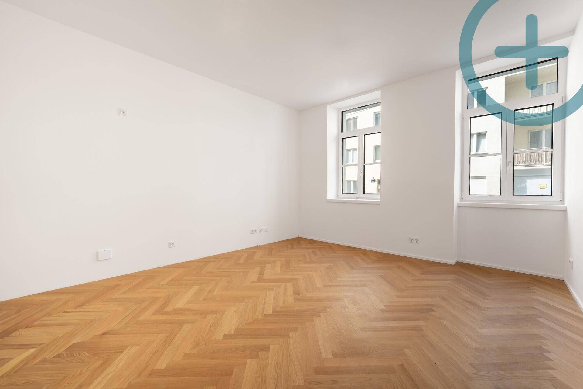 Geräumiges, helles Zimmer mit klassischem Fischgrätparkett und großen Fenstern.