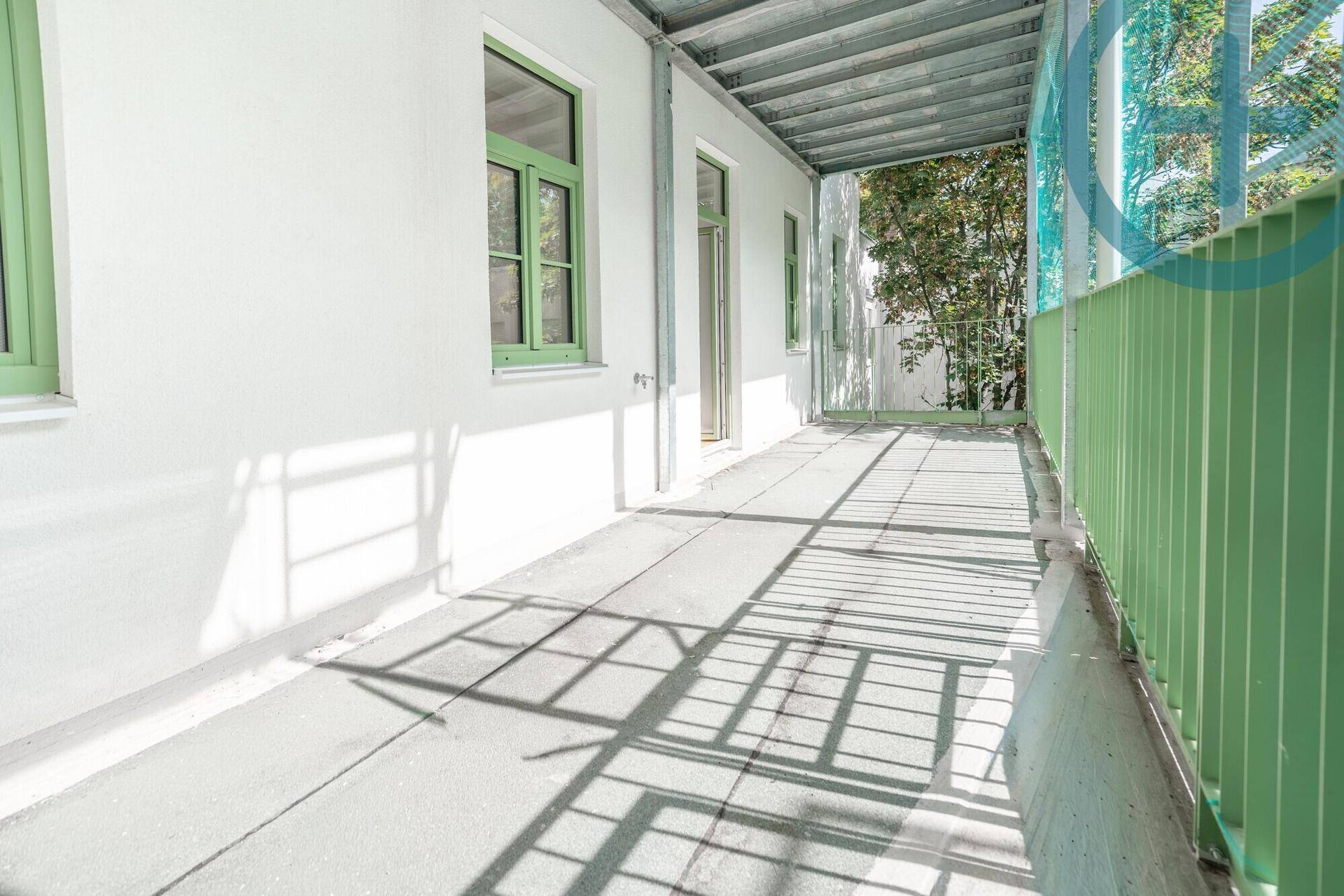 Überdachter Balkon mit grünen Akzenten und viel Sonnenlicht auf dem Boden.