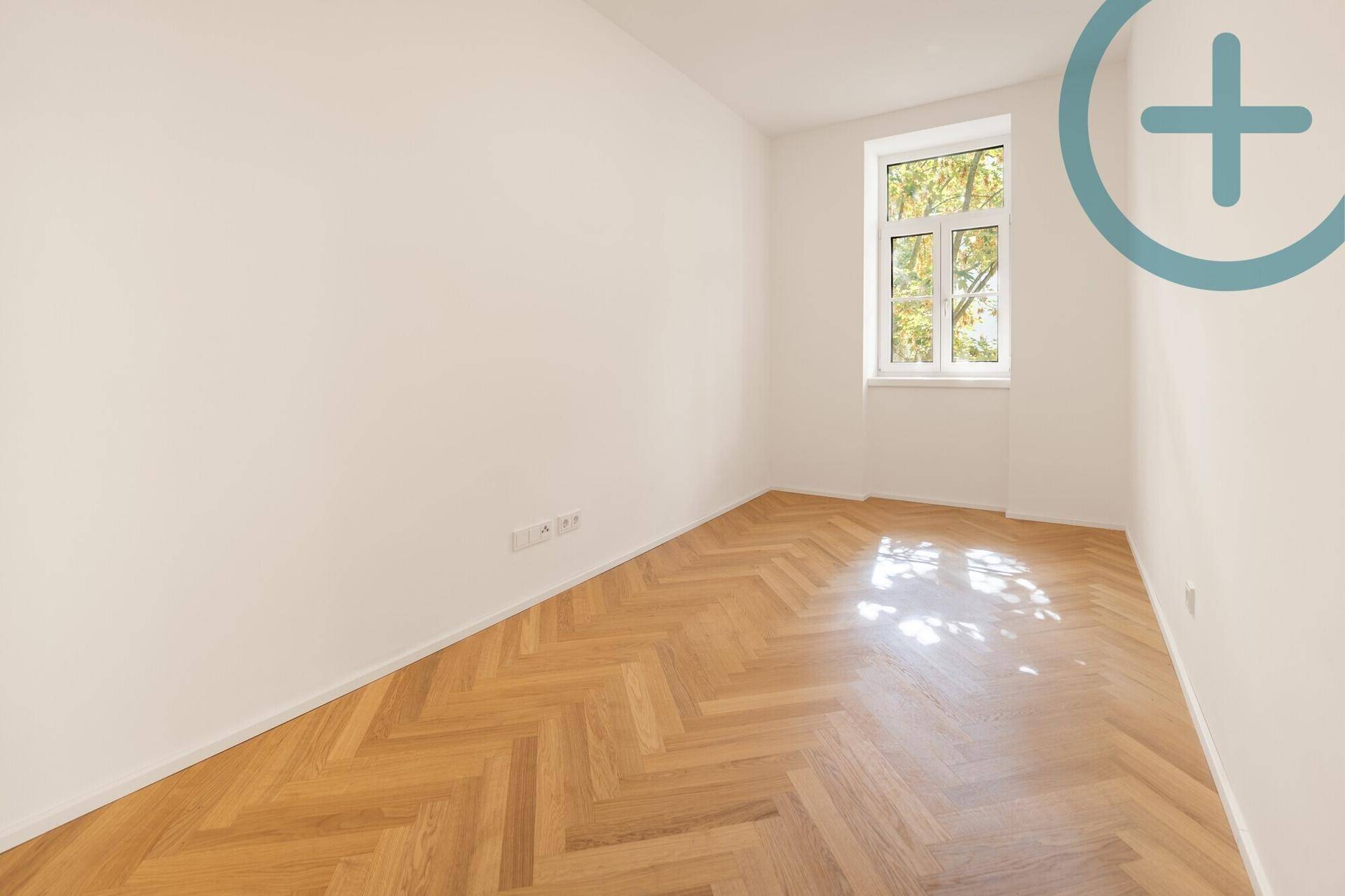 Leeres Zimmer mit Fischgrätparkett und einem Fenster, das viel natürliches Licht bietet.