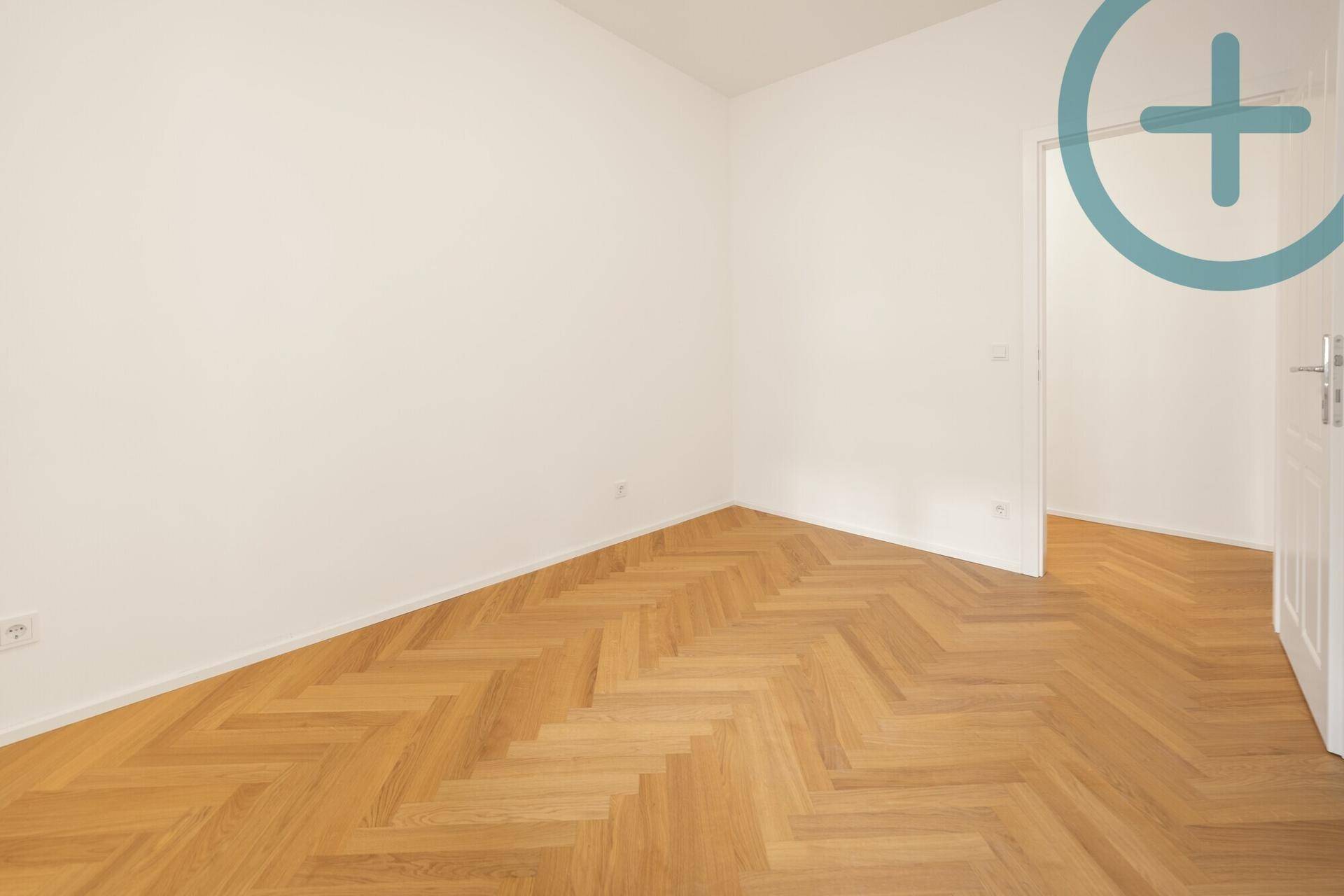 Leeres Zimmer mit Fischgrätparkett und einer offenen Tür, die den Zugang ermöglicht.
