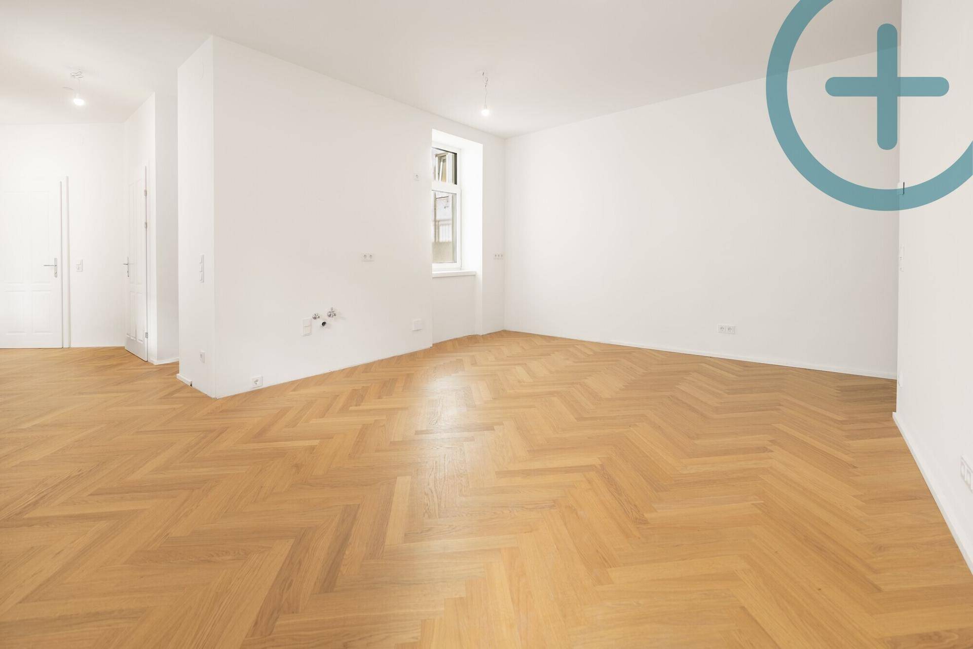 Leeres Zimmer mit Fischgrätparkett und einem Fenster, das viel Tageslicht hereinlässt.