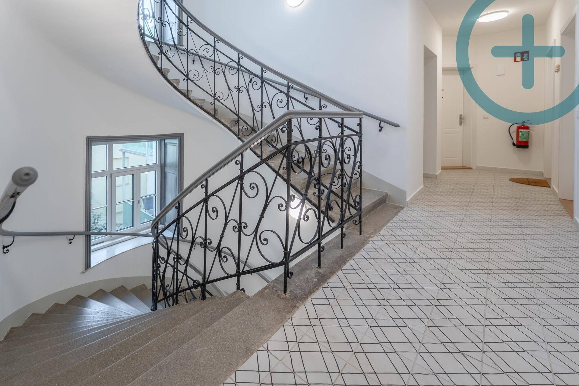 Elegantes Treppenhaus mit schmiedeeisernem Geländer und gemusterten Bodenfliesen.