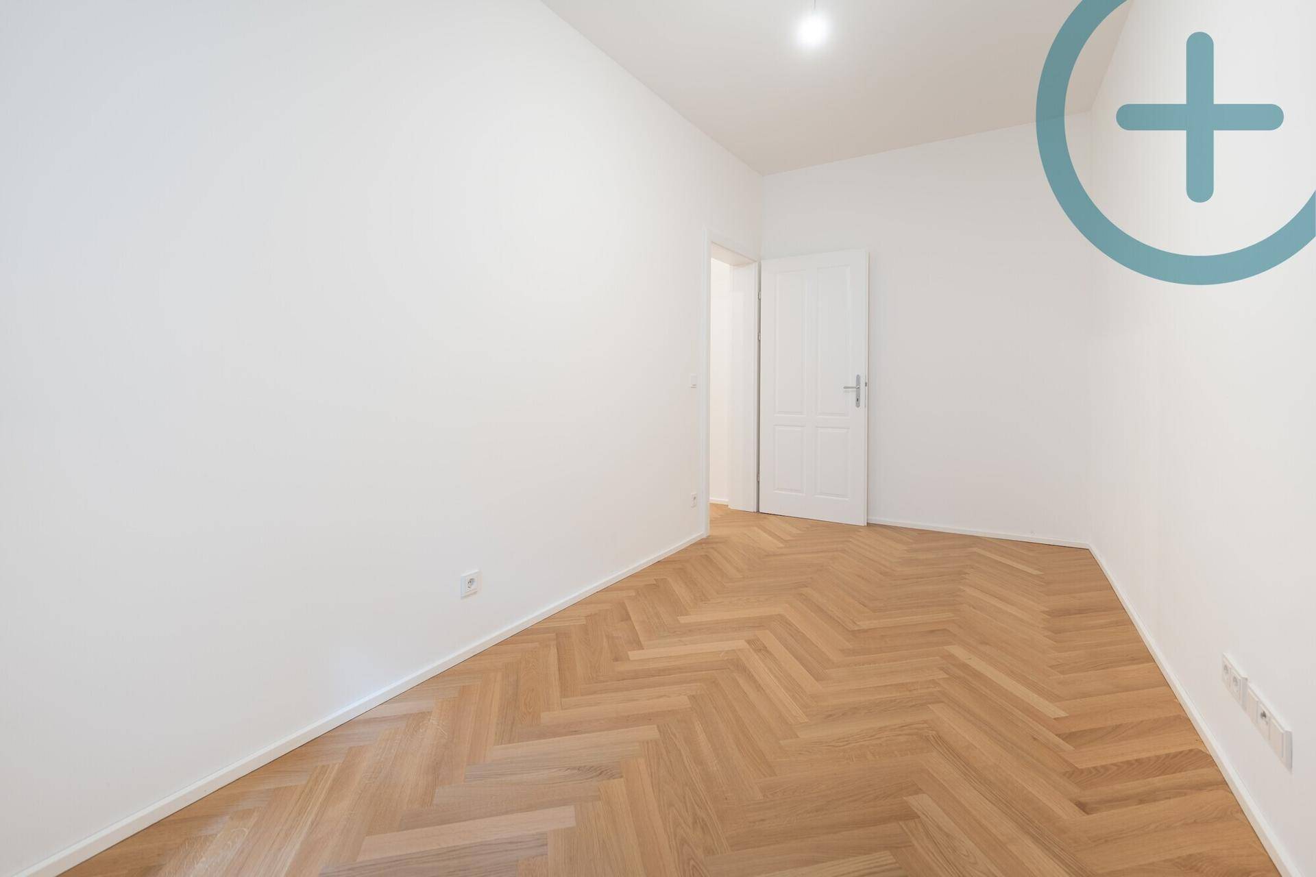 Leeres Zimmer mit Fischgrätparkett und weißer Tür, ideal für Schlaf- oder Kinderzimmer.
