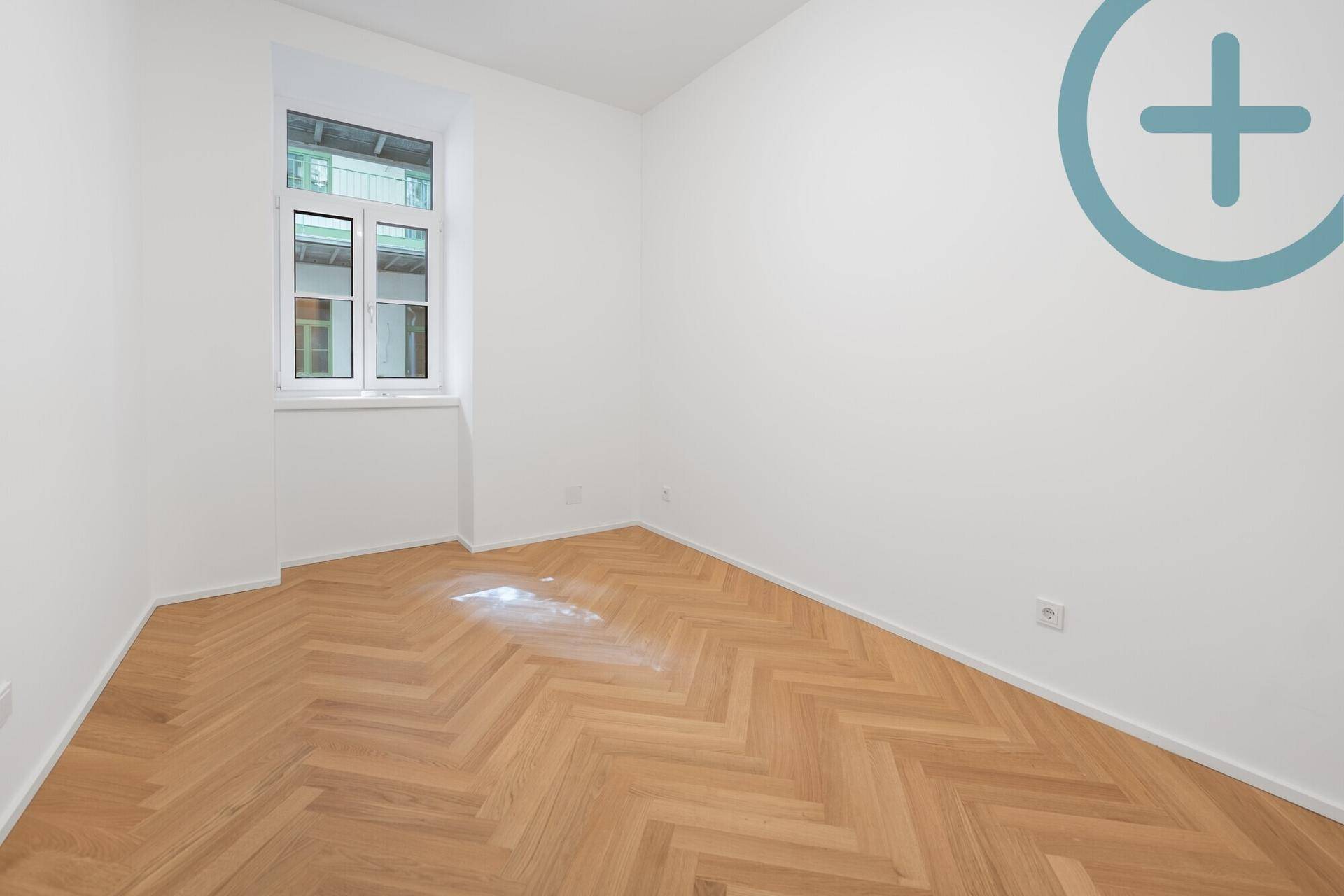 Helles Zimmer mit Fischgrätparkett und großem Fenster, ideal als Schlaf- oder Arbeitszimmer.