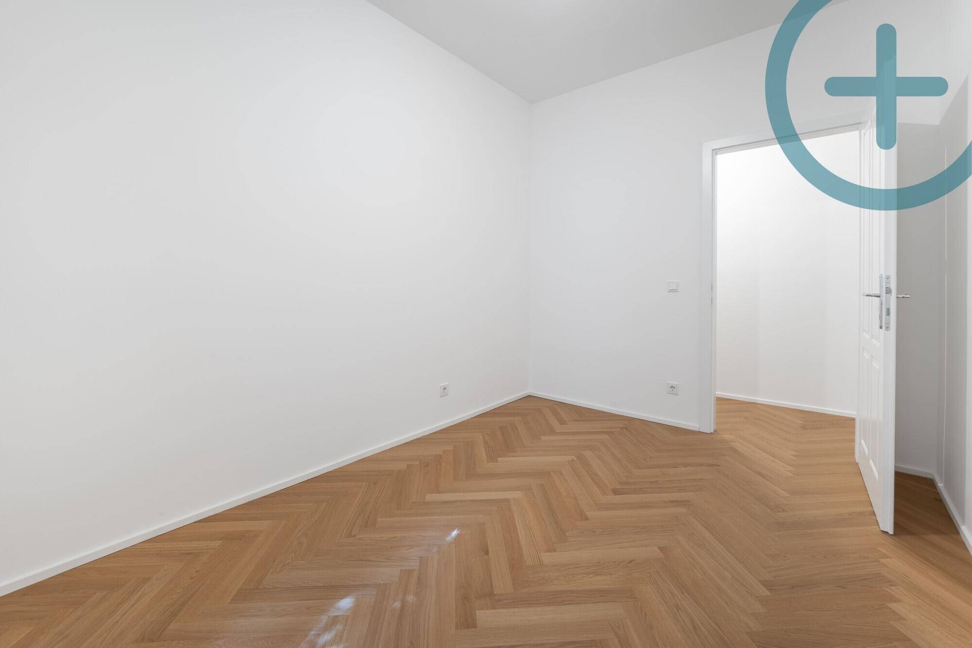 Leeres Zimmer mit Fischgrätparkett und weißer Tür, bietet vielseitige Nutzungsmöglichkeiten.