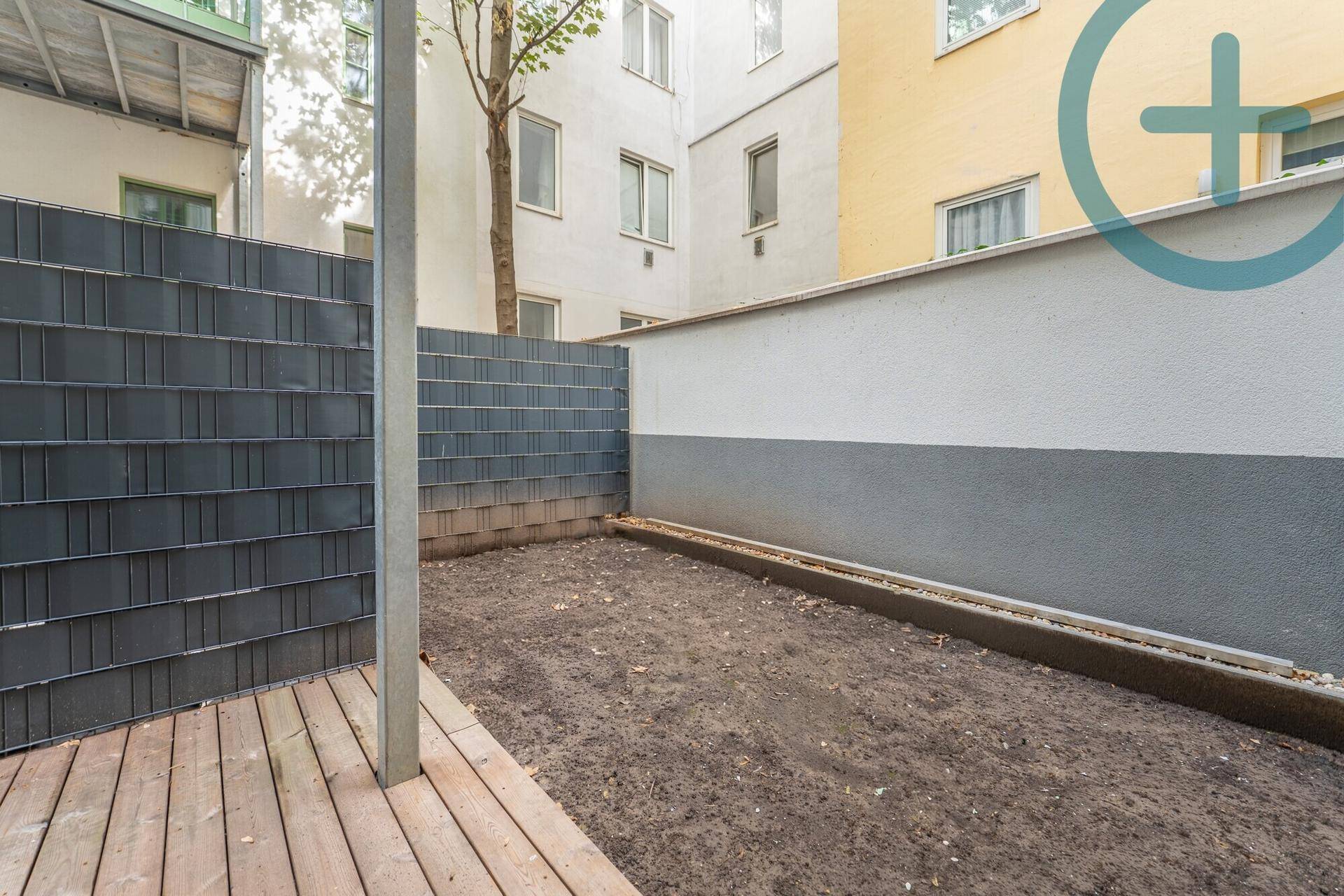 Kleiner Gartenbereich mit Holzterrasse und vorbereiteter Erde, umgeben von einer Hecke.