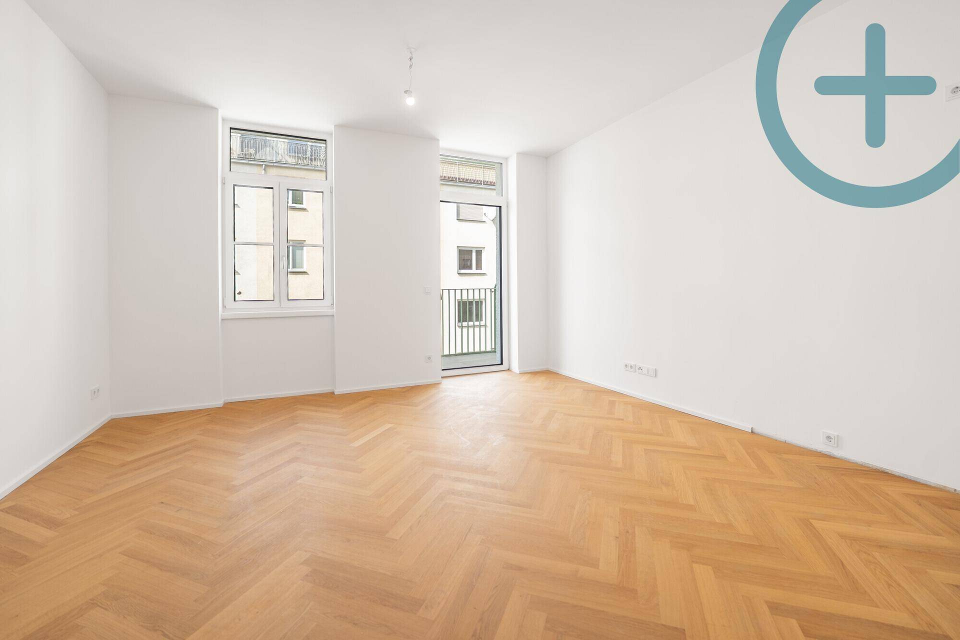 Lichtdurchflutetes Zimmer mit elegantem Fischgrätparkett und direktem Zugang zu einem französischen Balkon.