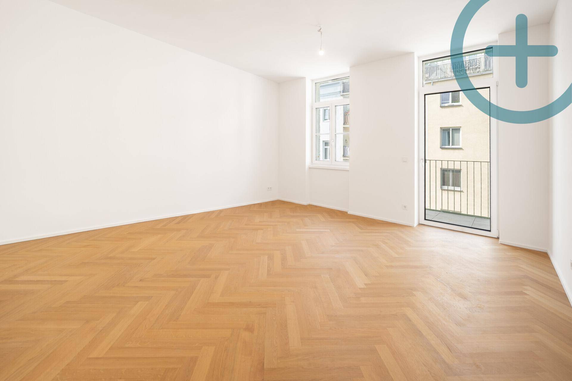 Geräumiges Zimmer mit hellem Fischgrätparkett, großen Fenstern und Zugang zum Balkon.