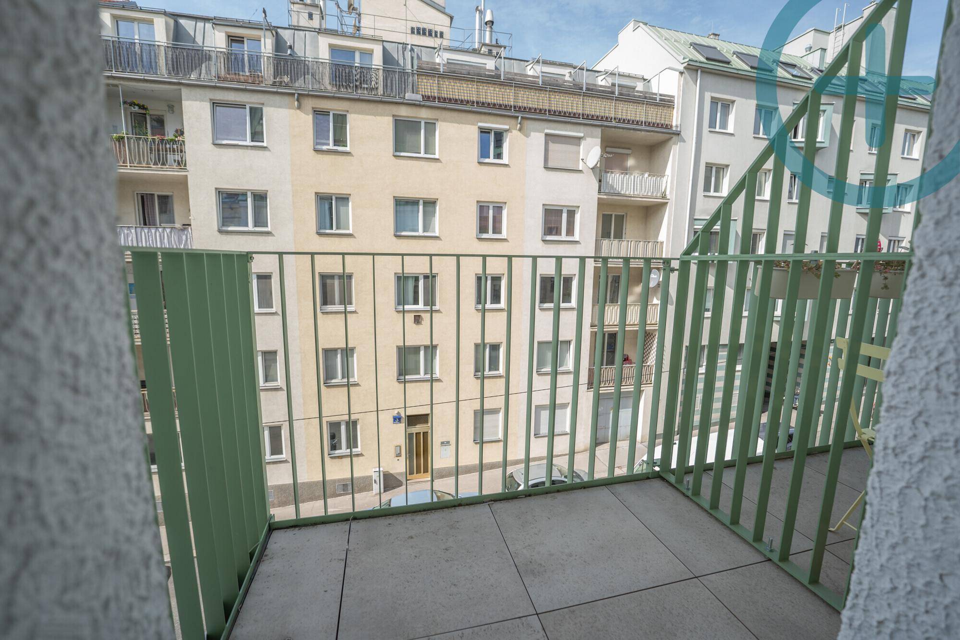 Balkon mit grüner Brüstung und Blick auf die umliegenden Gebäude und die Straße.