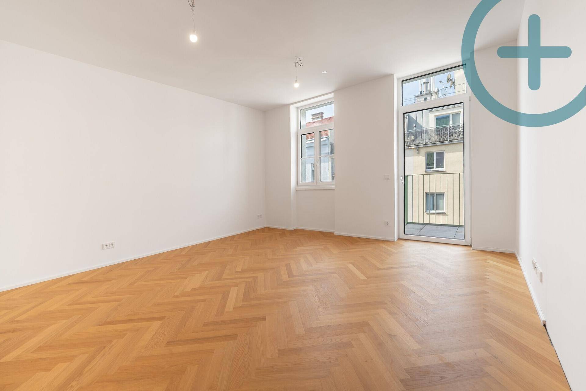 Geräumiges Zimmer mit hellem Fischgrätparkett und Blick auf die umliegenden Gebäude.