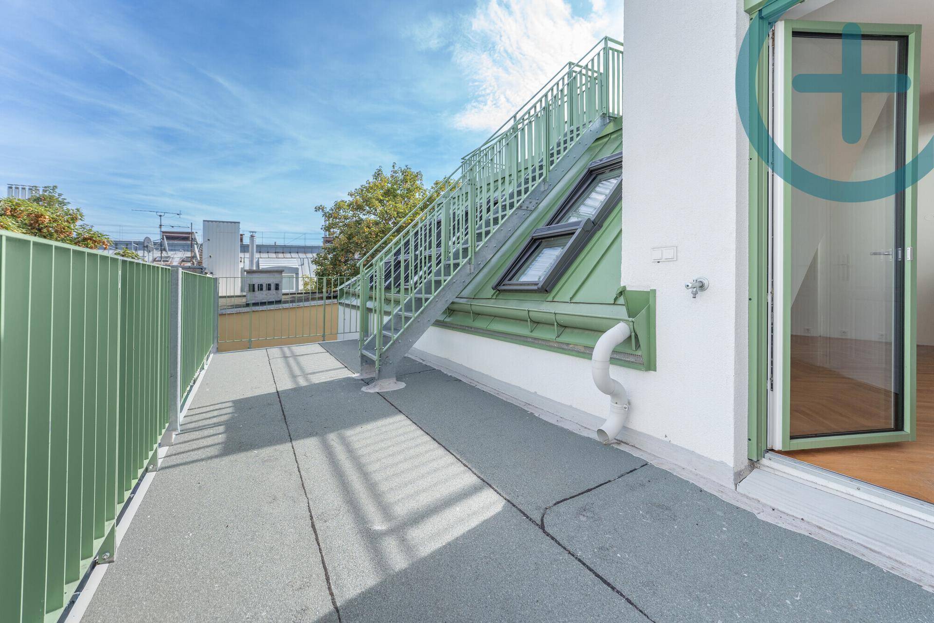Geräumige Dachterrasse mit grauem Bodenbelag und einer Metalltreppe zur oberen Ebene.