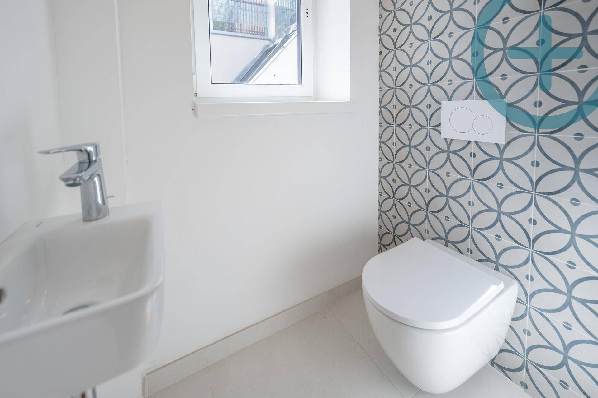 Gäste-WC mit dekorativen Fliesen, wandhängender Toilette, kleinem Waschbecken und Fenster.