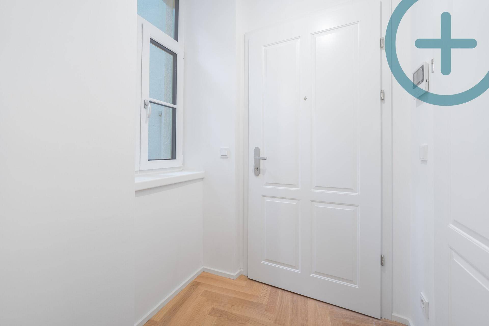 Heller Eingangsbereich mit Fischgrätparkett und weißer Tür, einladend und gepflegt.