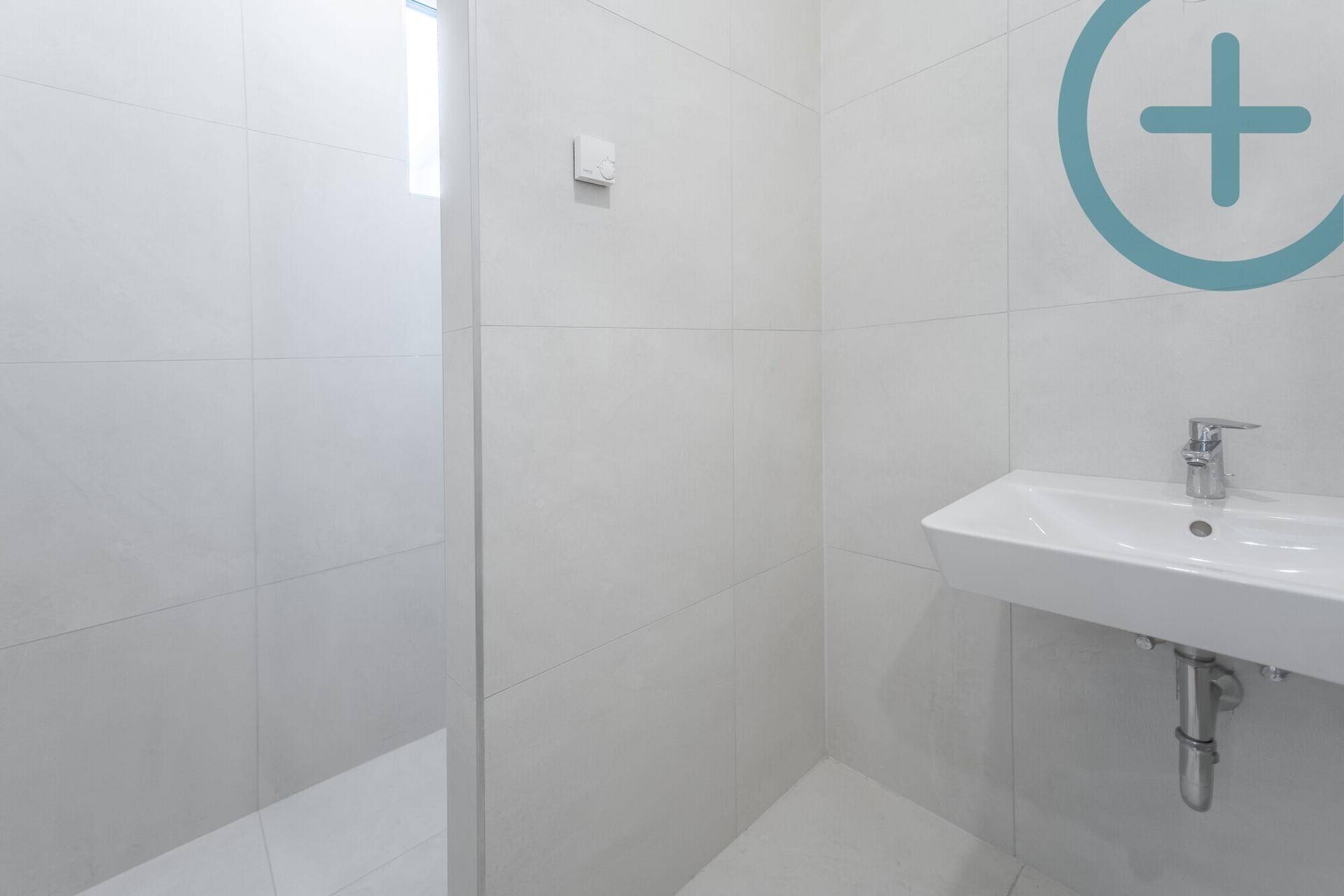 Modernes Badezimmer mit weißem Waschbecken, großen Fliesen und Duschbereich.
