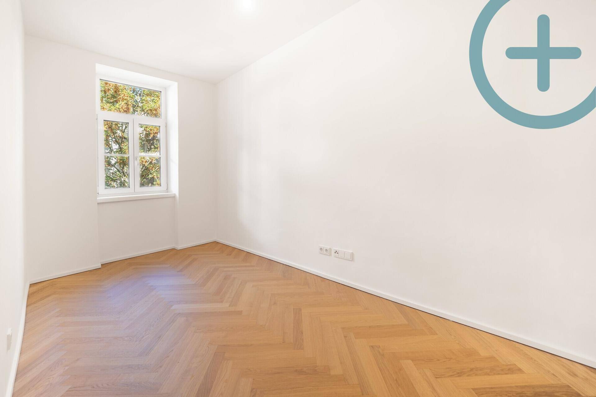 Unmöbliertes Zimmer mit Fischgrätparkett und viel Tageslicht durch das große Fenster.