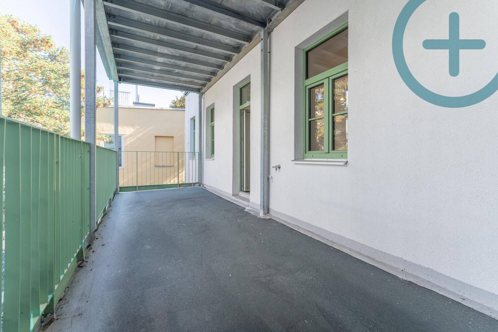 Langer, überdachter Balkon mit grünem Geländer und Ausblick ins Grüne.