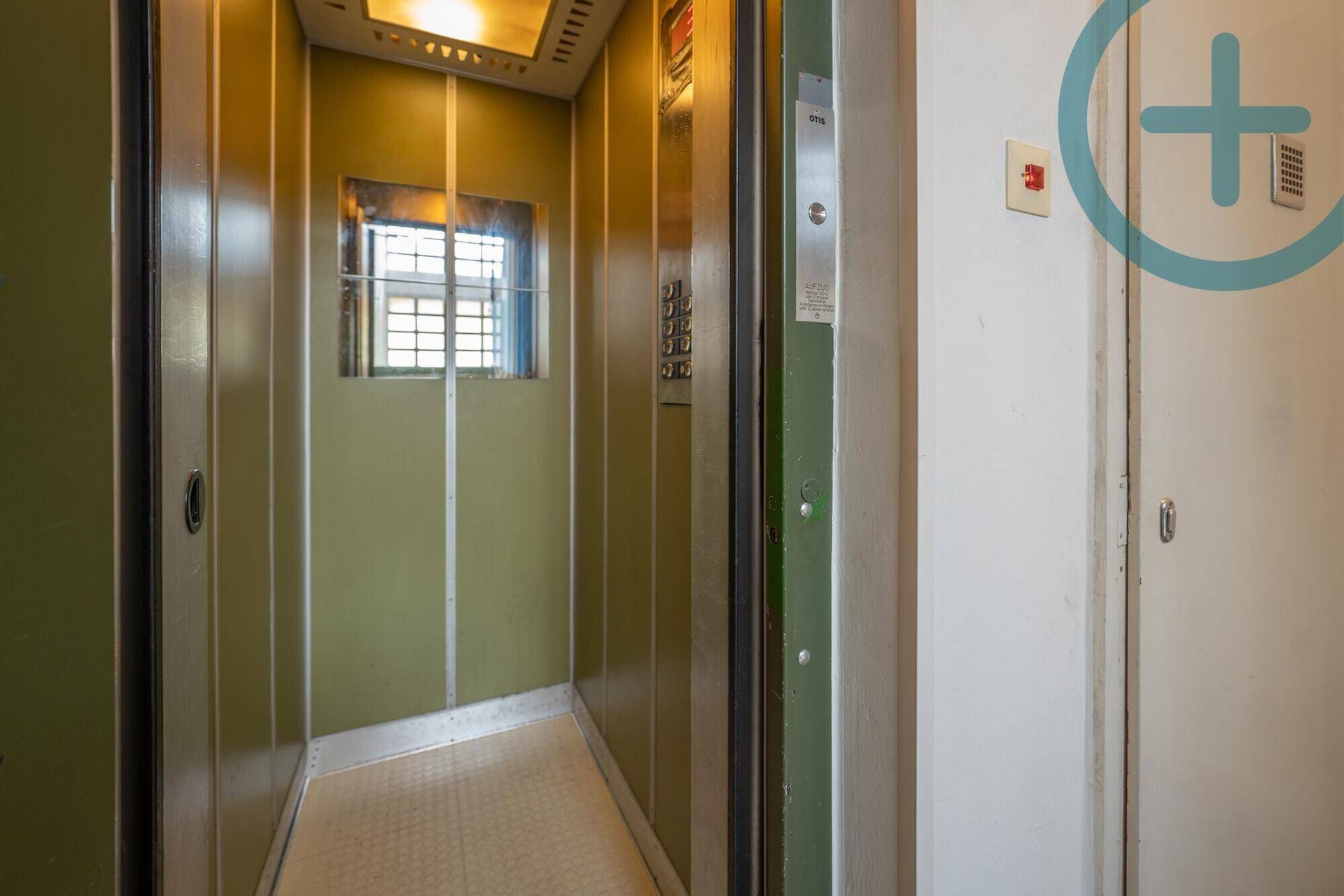 Alter Aufzug mit grünen Paneelen und einem kleinen Fenster, im Gemeinschaftsbereich des Gebäudes.