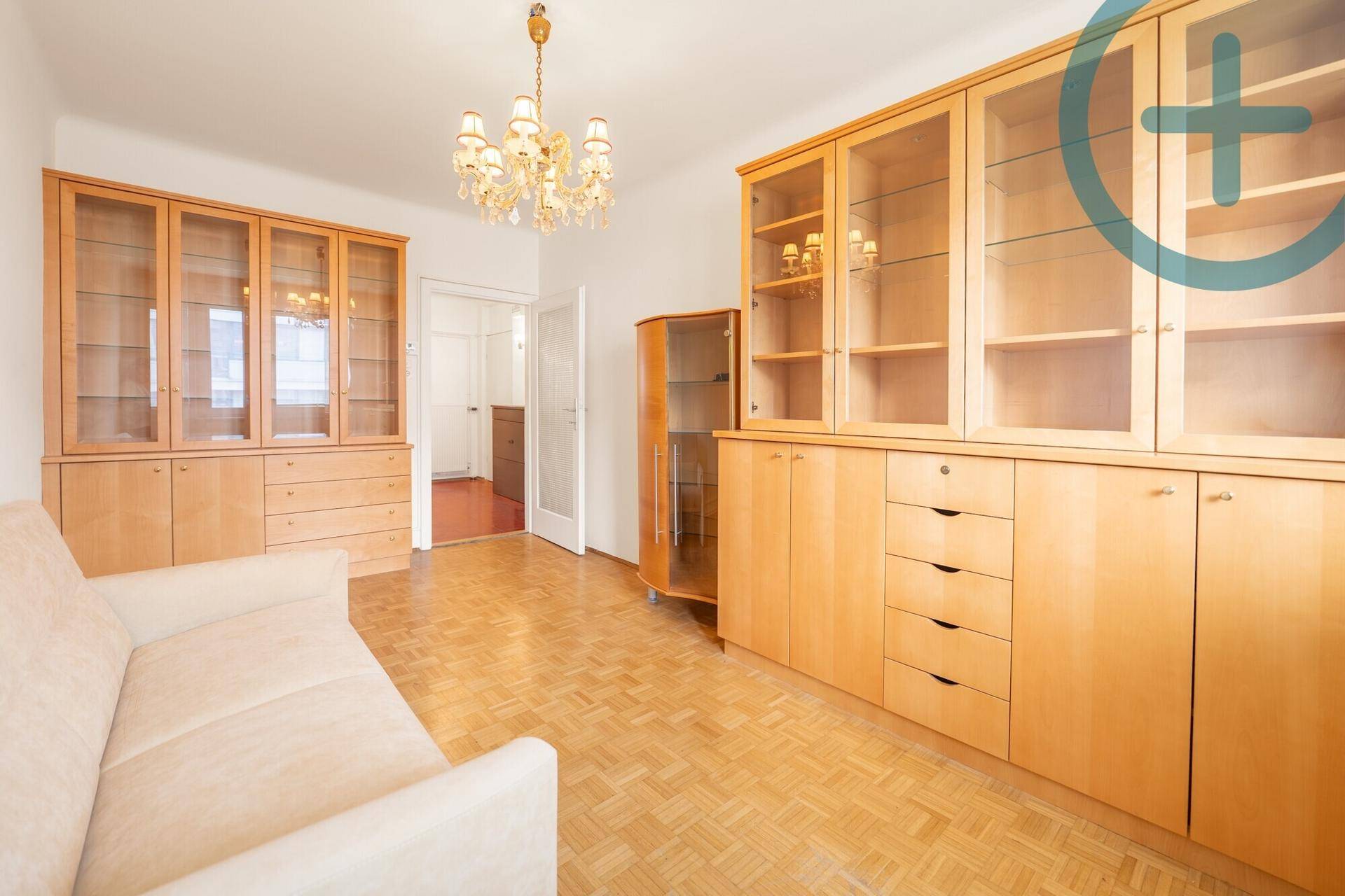 Geräumiges Wohnzimmer mit umfangreichen Holzvitrinen, Sofa und Kronleuchter, gut beleuchtet.