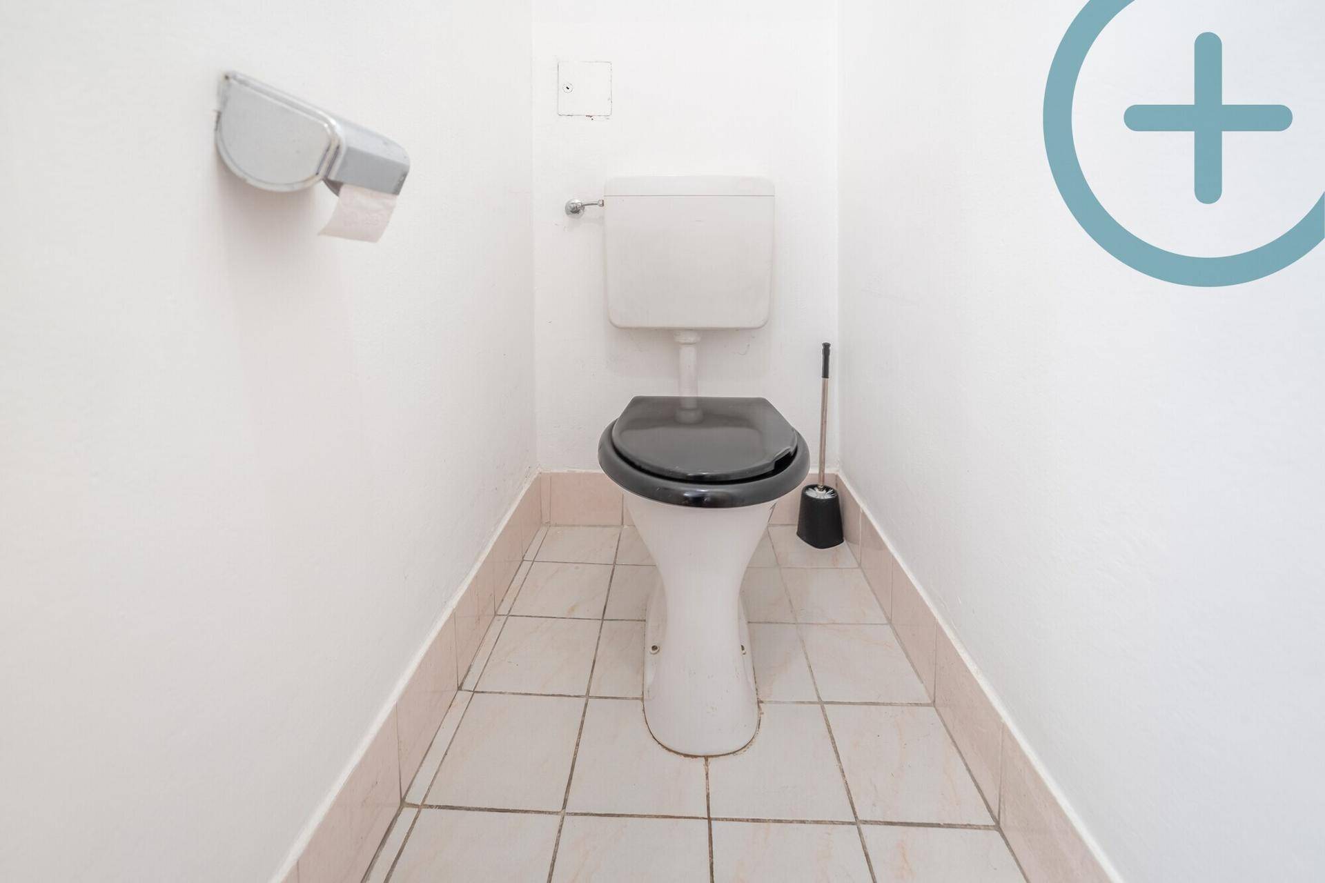 Kleines separates WC mit weißer Toilette und hellen Fliesen an Boden und Wänden.