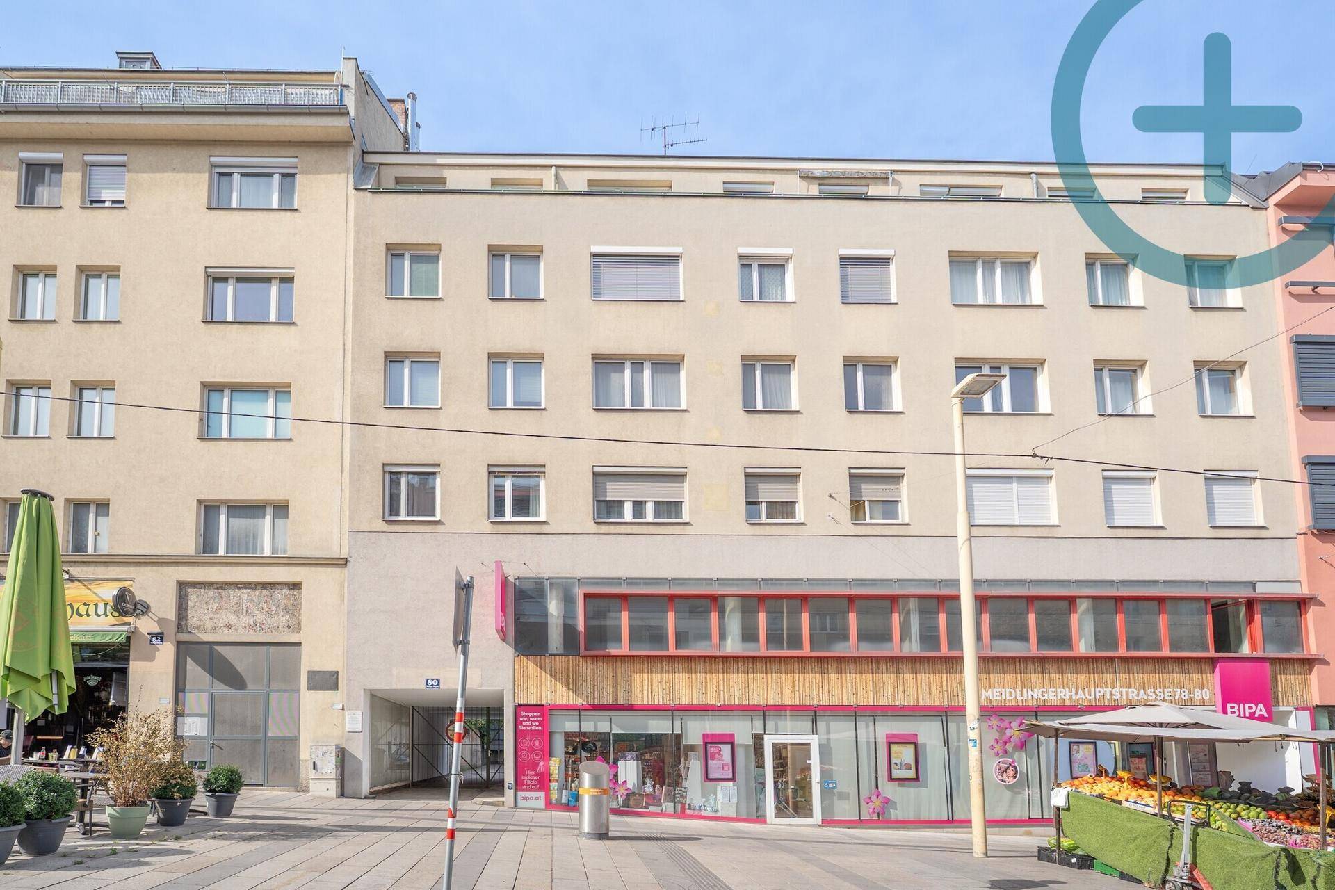Fassade eines Mehrfamilienhauses mit Geschäften im Erdgeschoss an einer belebten Straße.