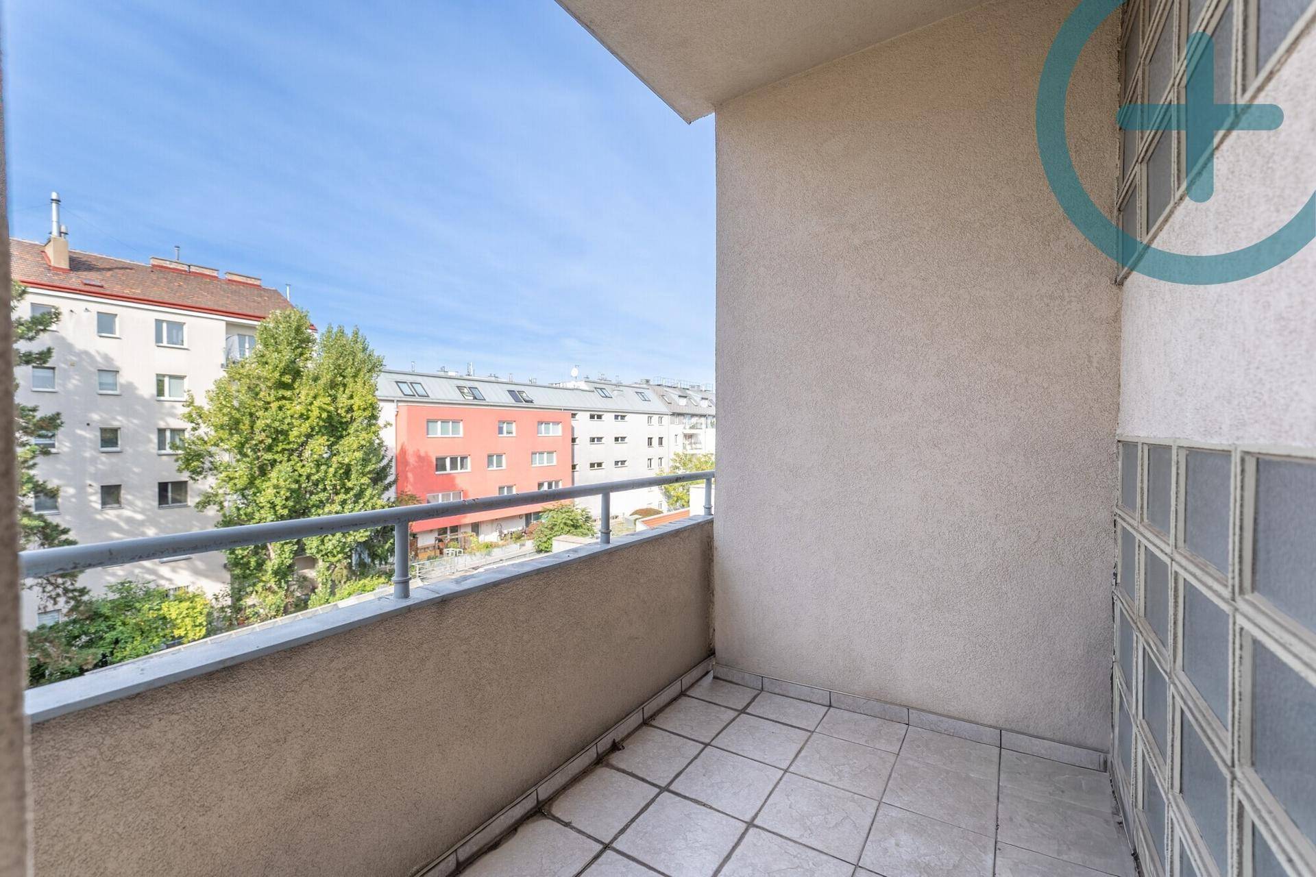 Balkon mit Fliesenboden und Blick auf die umliegenden Wohngebäude und Bäume.