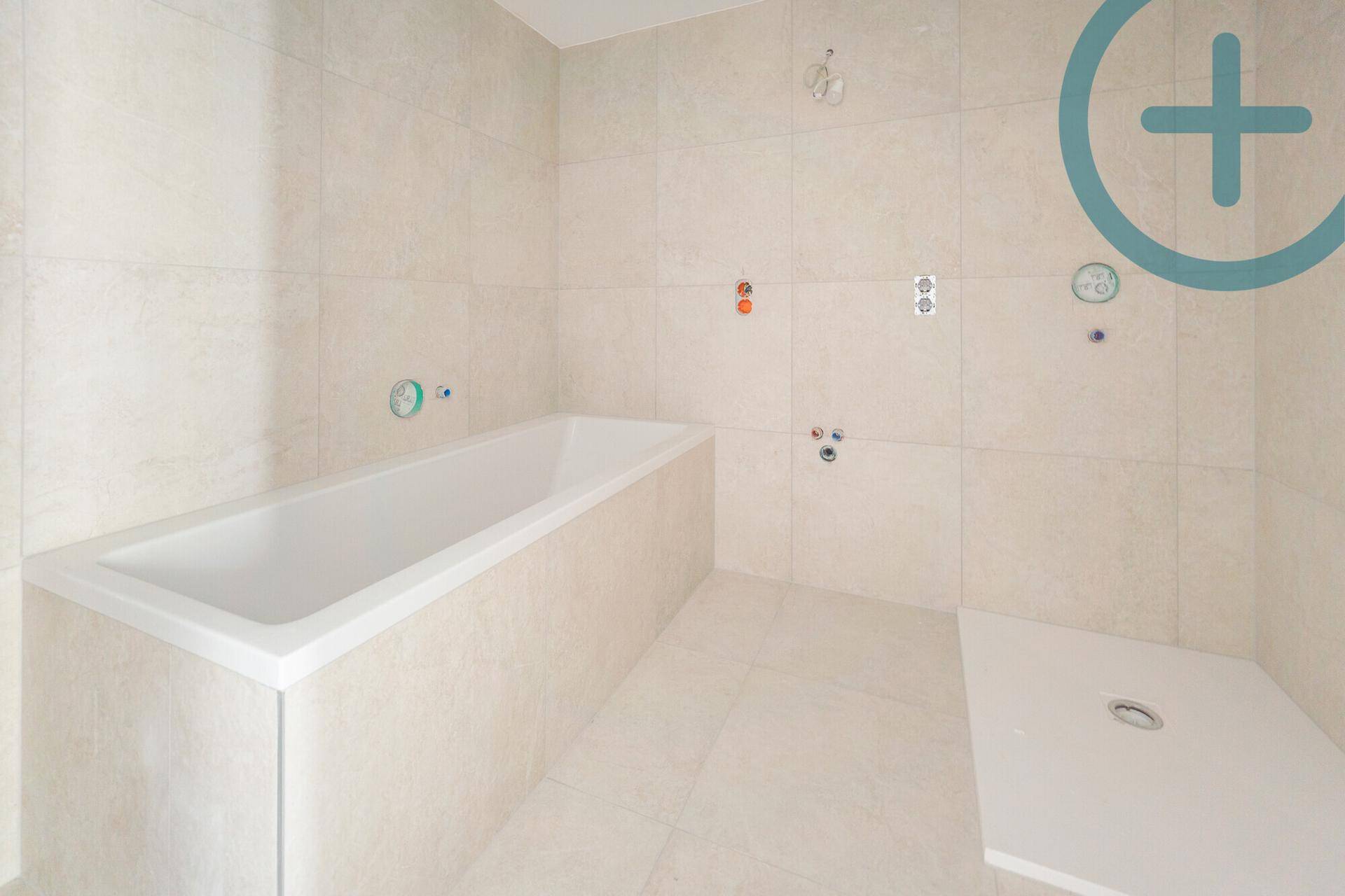Modernes Badezimmer im Rohbau mit hellen Fliesen, Badewanne und begehbarer Dusche.