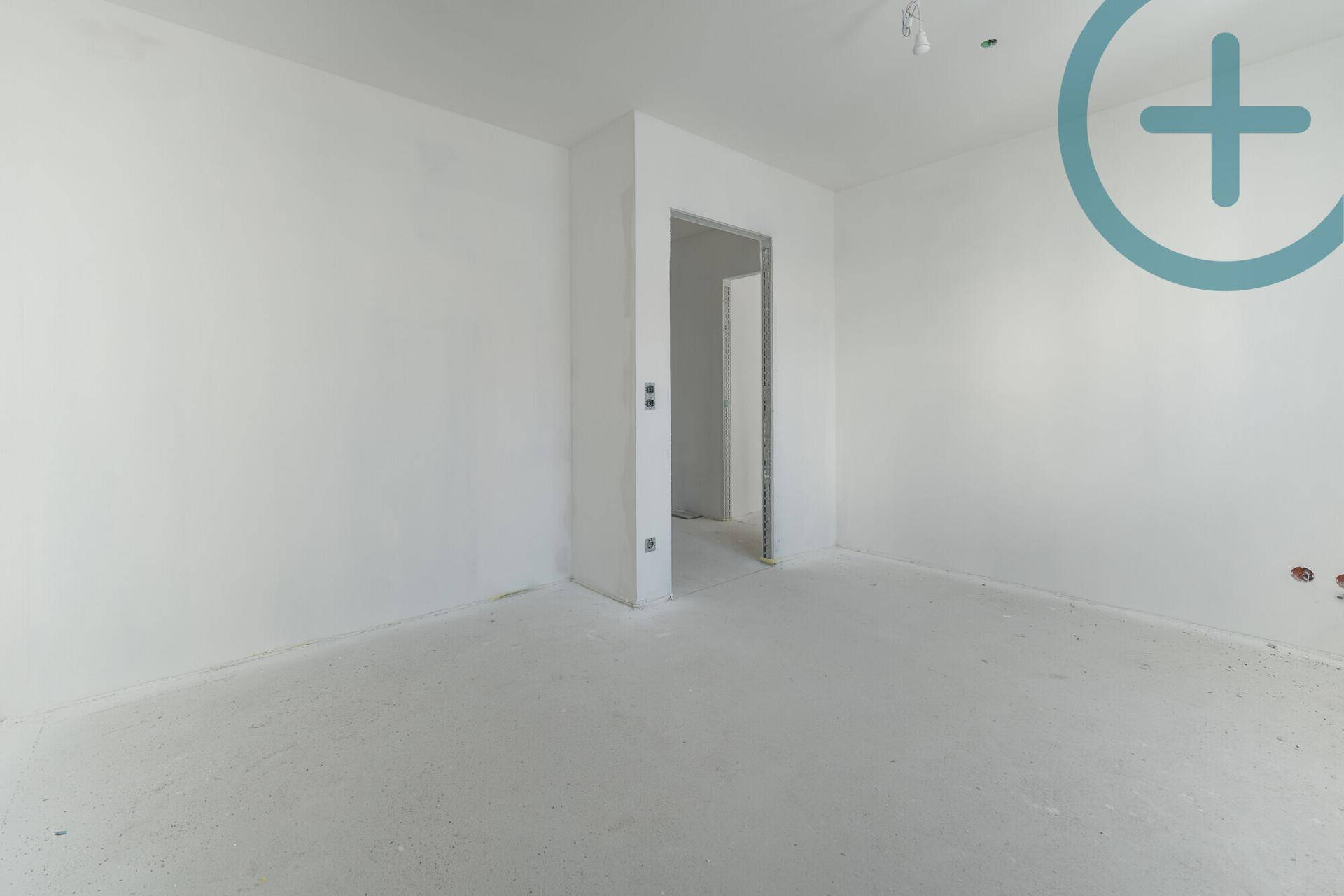 Leerer Raum im Rohbau mit Betonboden und einem offenen Durchgang zu einem weiteren Zimmer.
