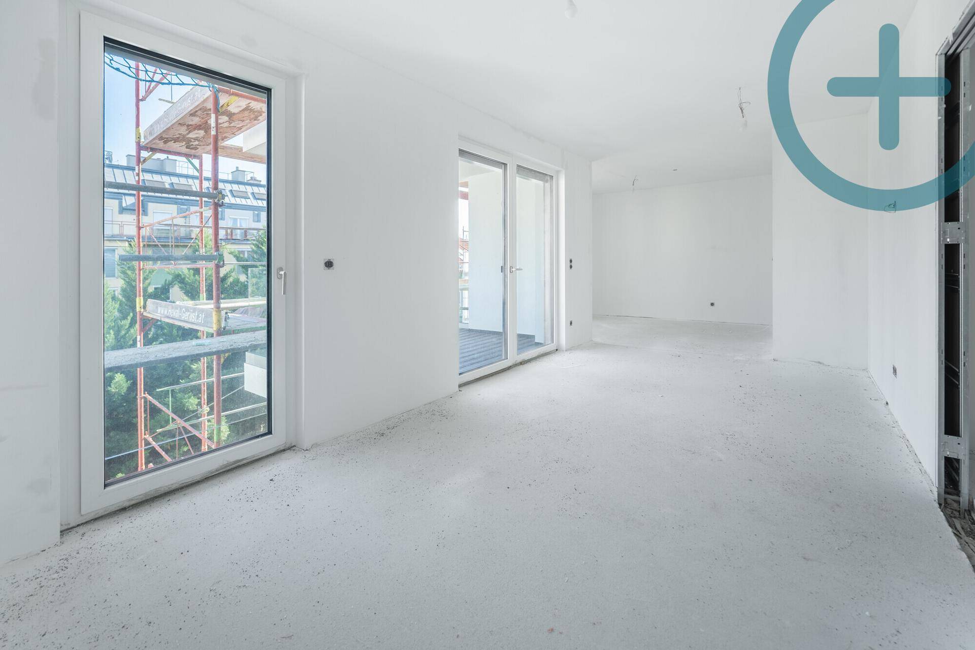 Unfertiger Raum im Rohbau mit Betonboden, weißen Wänden und großen Fenstern zum Balkon.