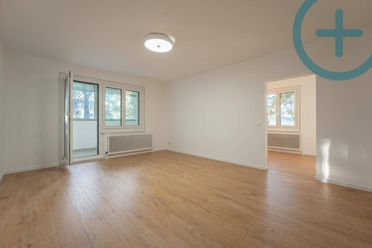 Geräumiges Wohnzimmer mit hellem Laminatboden und viel Tageslicht durch große Fenster.