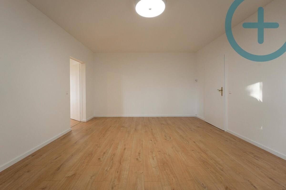 Geräumiges, unmöbliertes Zimmer mit Laminatboden und weiß gestrichenen Wänden.