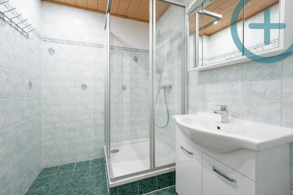 Badezimmer mit Duschkabine, Waschbecken und hellblauen Fliesen.