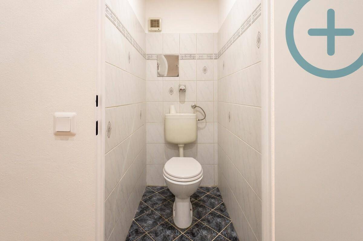 Separate Toilette mit WC, kleinem Waschbecken und Fliesenboden.