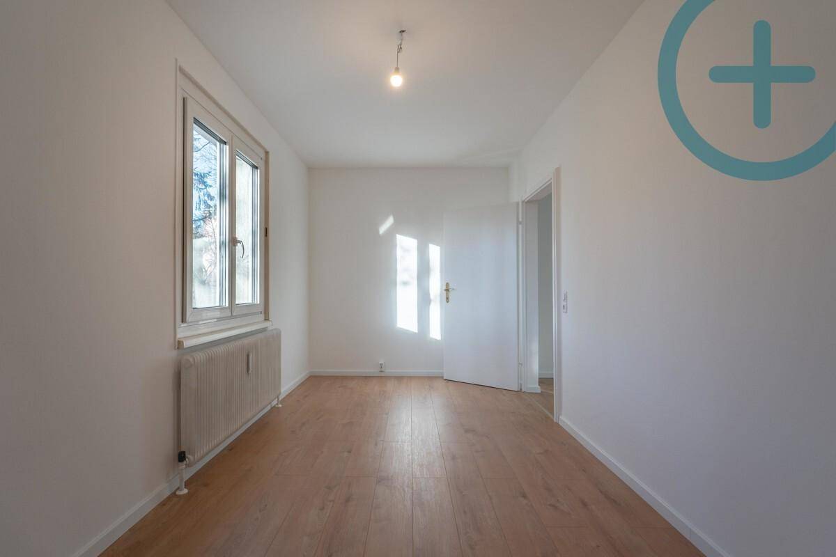 Leeres Zimmer mit Laminatboden, weiß gestrichenen Wänden und natürlichem Lichteinfall.