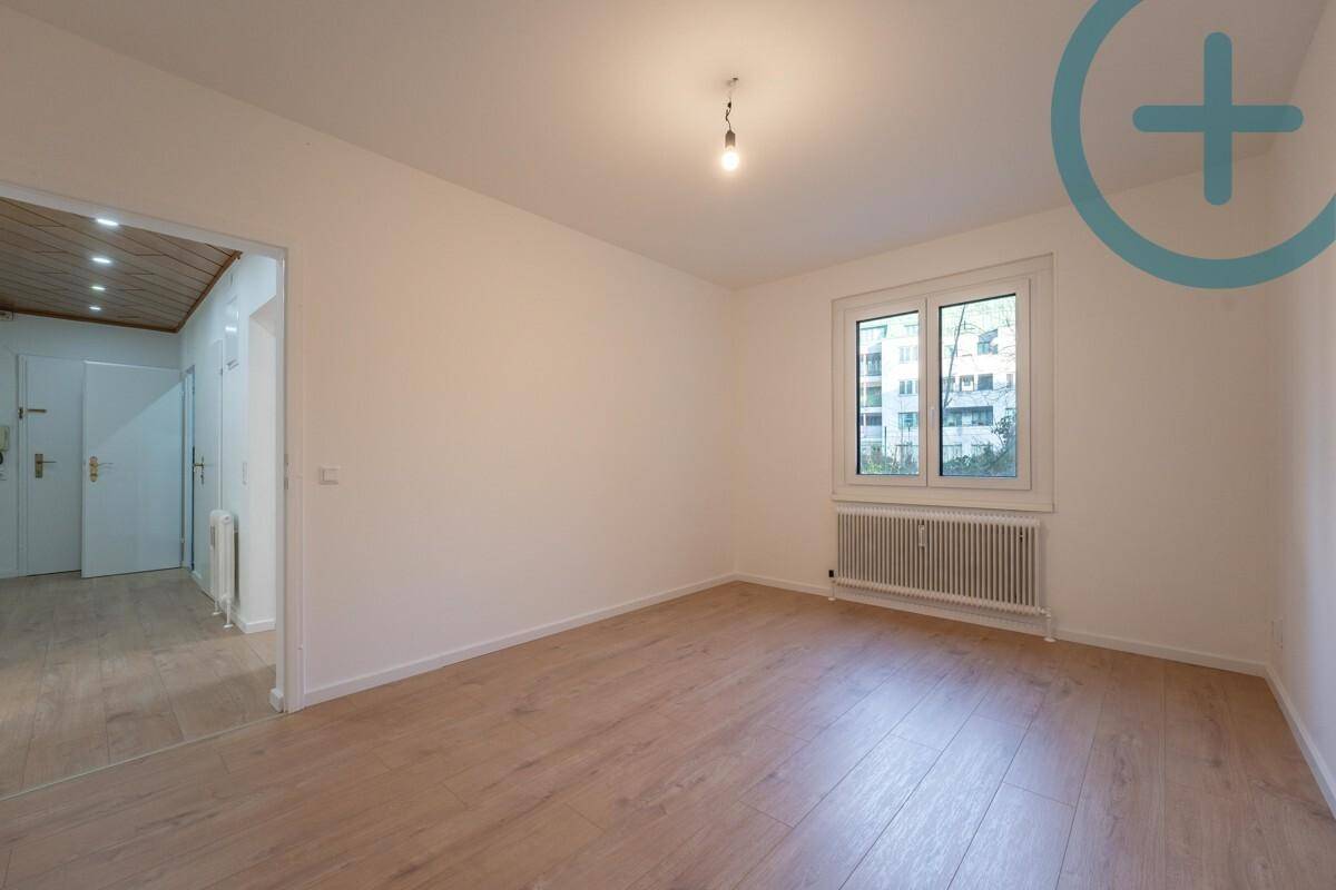 Leeres Zimmer mit Laminatboden und einem Fenster, das viel Licht hereinlässt.