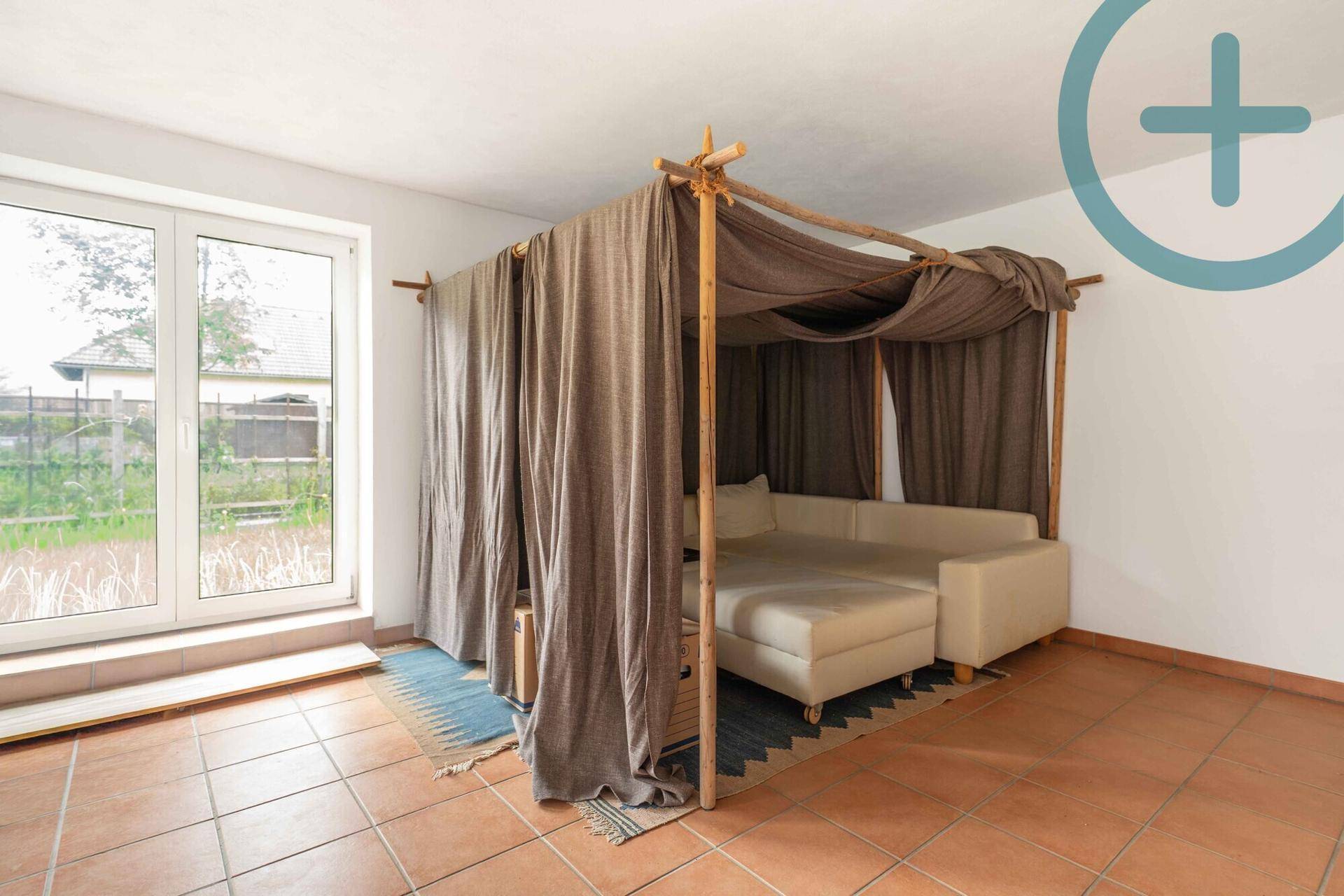 Gemütliches Zimmer mit Himmelbett, Terrakottafliesen und Zugang zum Außenbereich durch große Fenster.