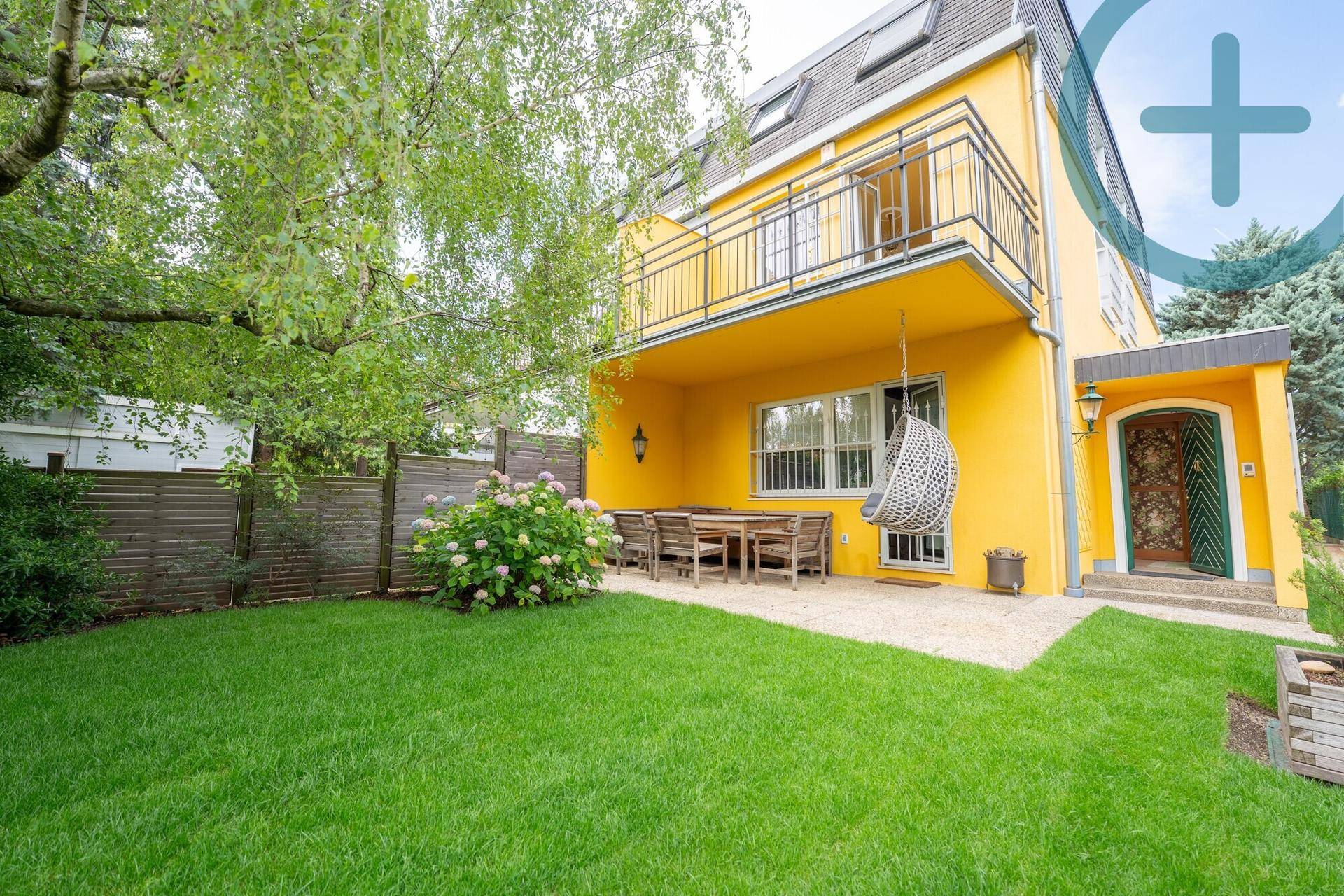 Gepflegter Gartenbereich mit Terrasse, Rasenfläche und einem Balkon am gelben Haus.