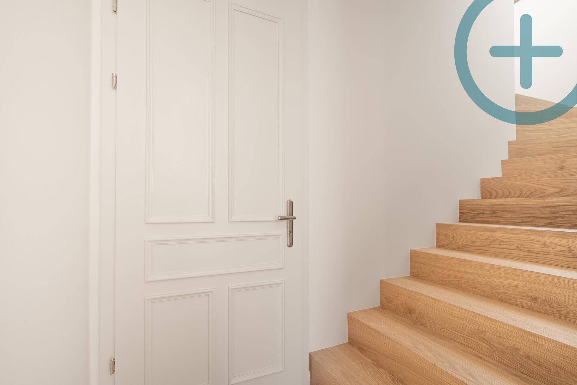 Weiße Kassettentür neben einer eleganten Holztreppe in einem hellen Flur.