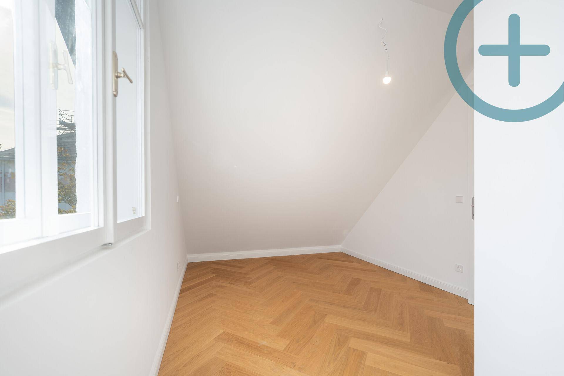 Kleineres Zimmer mit Fischgrätparkett, Dachschräge und hellem Fenster.