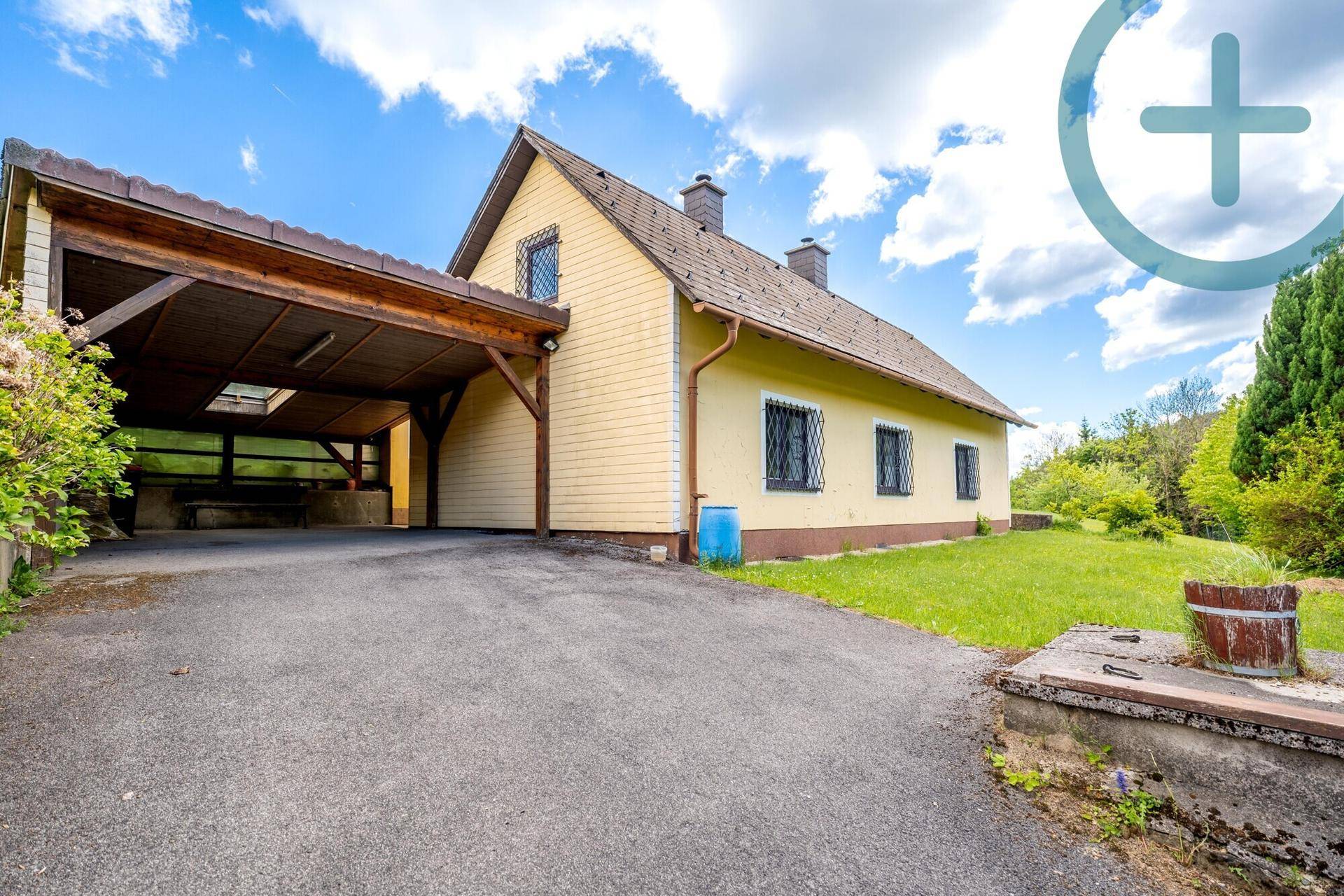 Gelbes Einfamilienhaus mit Holzcarport und Zufahrt unter blauem Himmel.