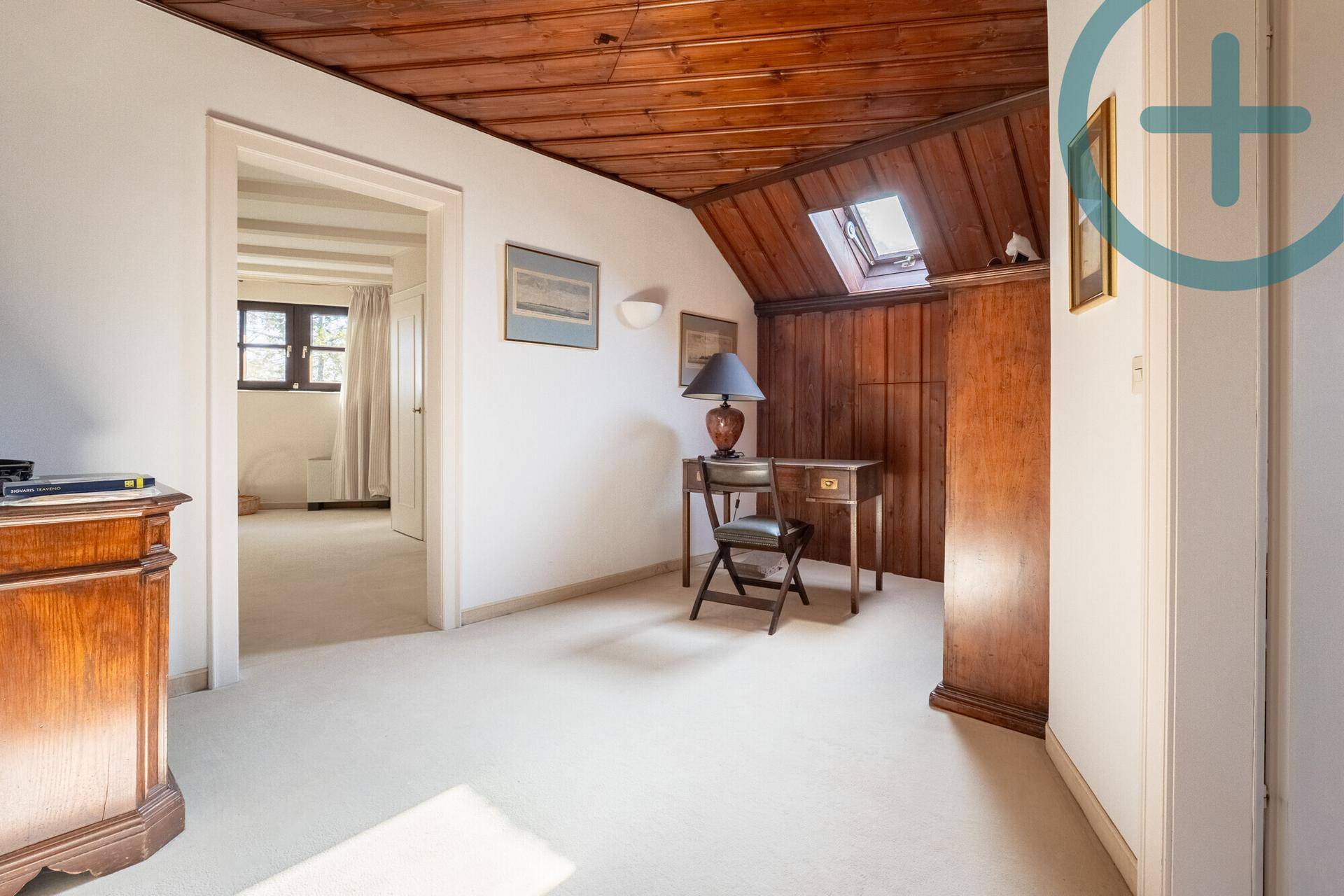 Dachgeschosszimmer mit Holzdachschrägen, Teppichboden und kleinem Schreibtischbereich.