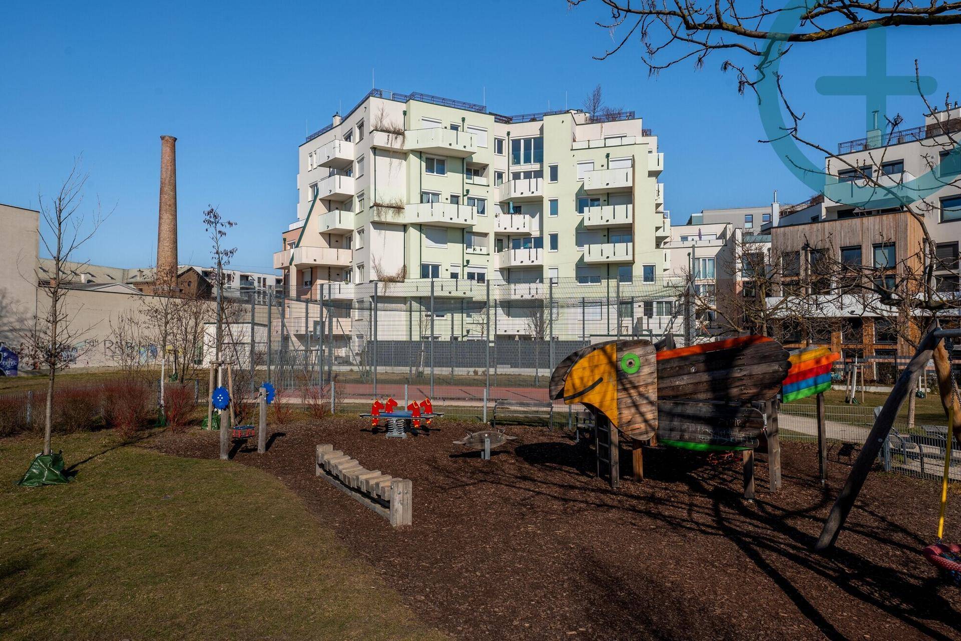 Spielplatz mit verschiedenen Spielgeräten und einem modernen Wohngebäude im Hintergrund.