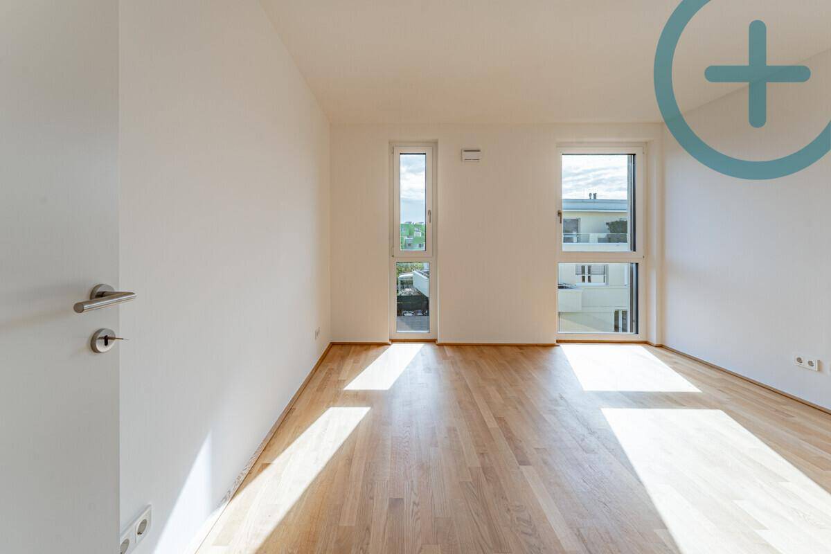 Lichtdurchflutetes Zimmer mit Parkettboden und zwei hohen Fenstern in einem Neubau.