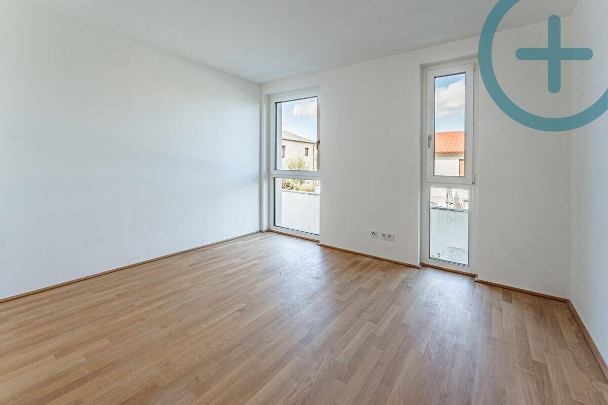 Helles Zimmer mit Parkettboden und zwei großen Fenstern, eines mit französischem Balkon.
