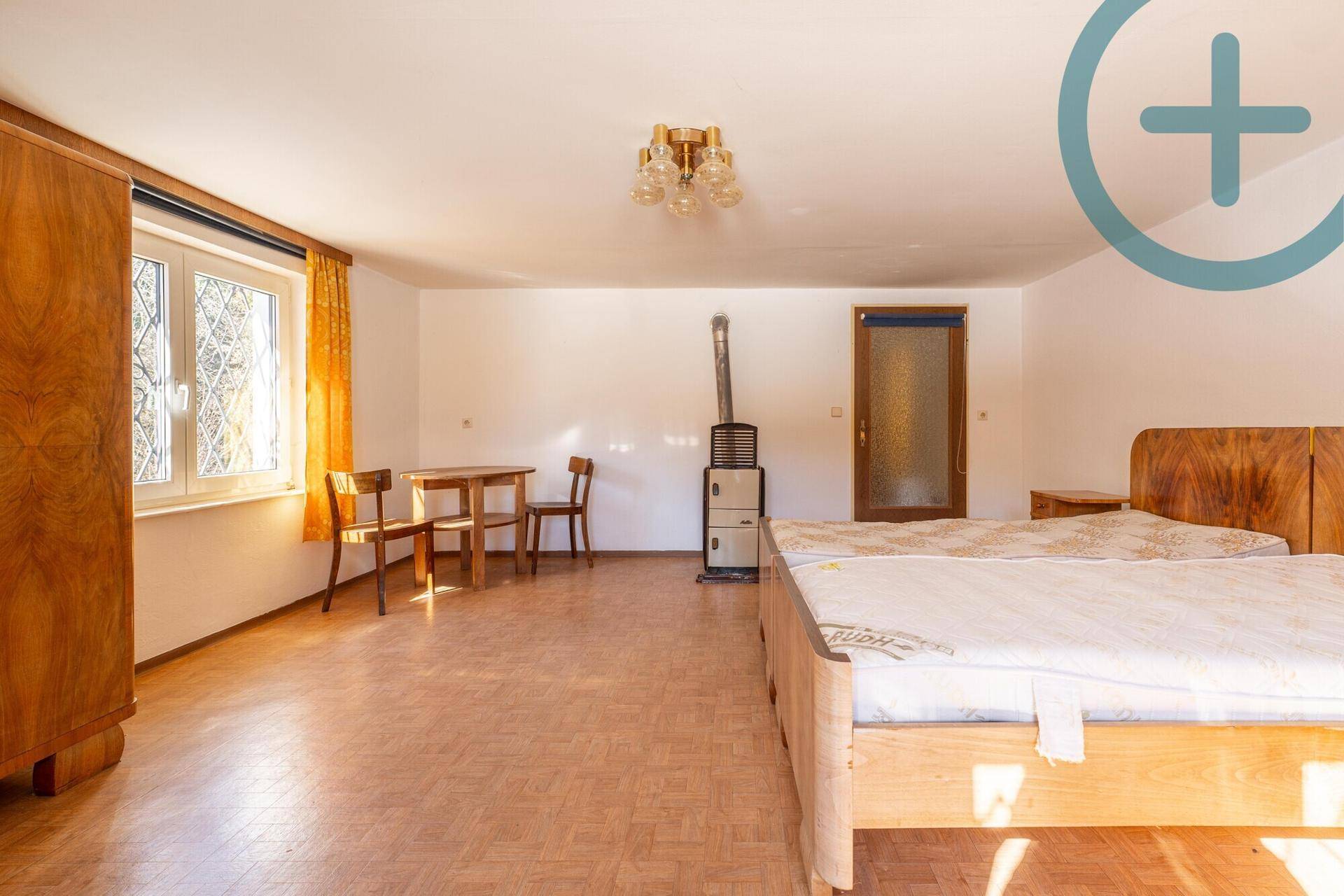 Helles Schlafzimmer mit zwei Betten, Holzschrank und einem traditionellen Ofen.