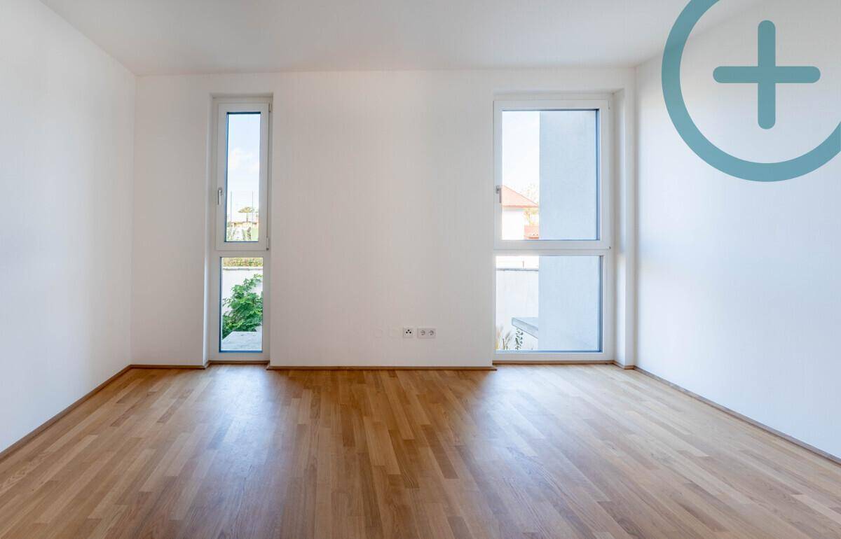 Helles Schlafzimmer mit Parkettboden und zwei hohen Fenstern, die viel Tageslicht bieten.