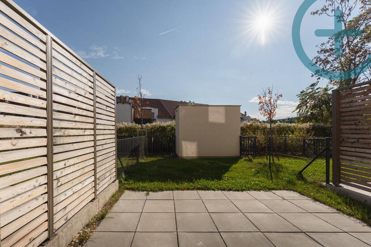 Sonniger Terrassenbereich mit Pflastersteinen und kleinem Rasen, umgeben von Holzzäunen für Privatsphäre.